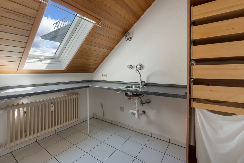 Dachzimmer mit Dachfenster, Waschbecken, Heizung und Holzdecke, weiße Fliesen am Boden.