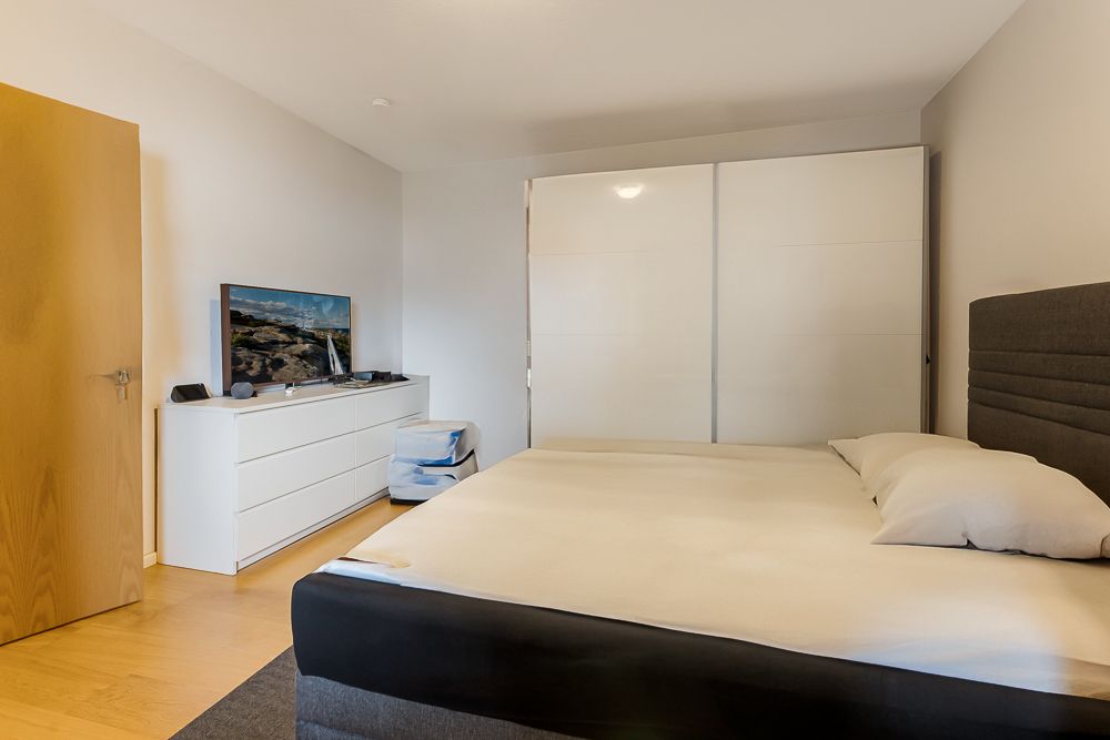 Schlafzimmer mit Doppelbett, weißem Kleiderschrank und Kommode mit Fernseher.