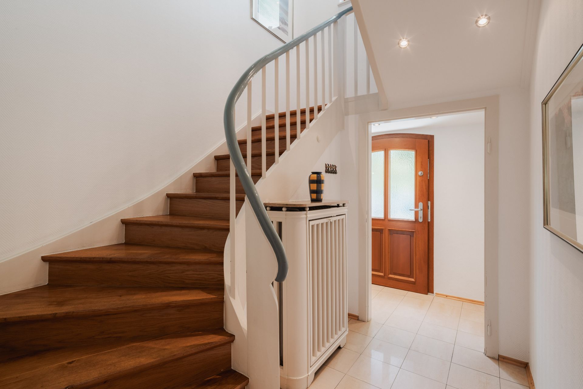 Heller Flur mit Holztreppe und brauner Haustür.