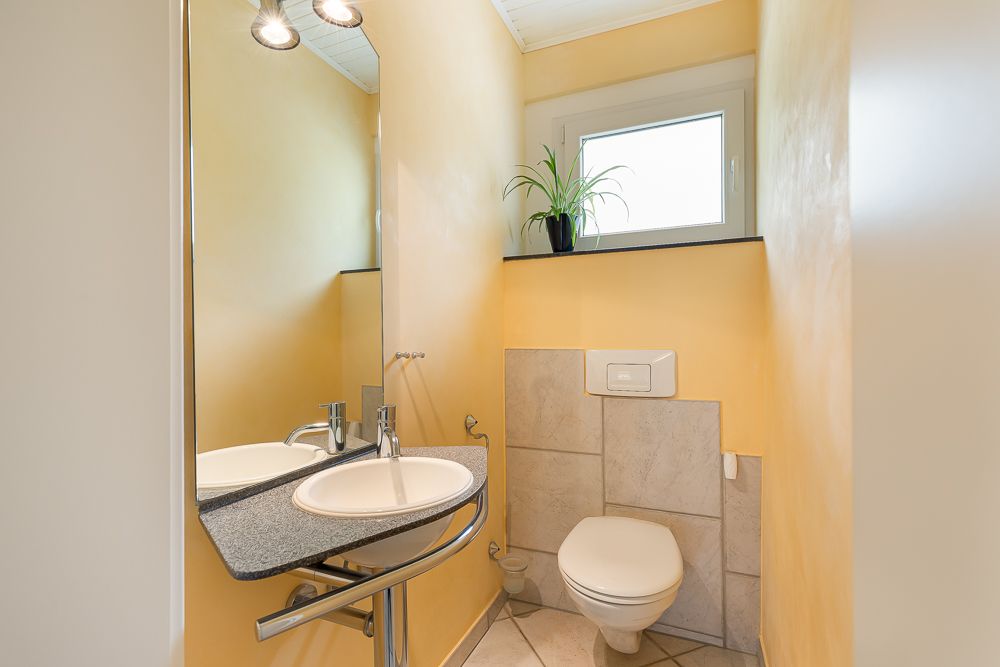 Kleines Badezimmer mit Waschbecken, Spiegel, Toilette und Pflanze auf dem Fensterbrett.