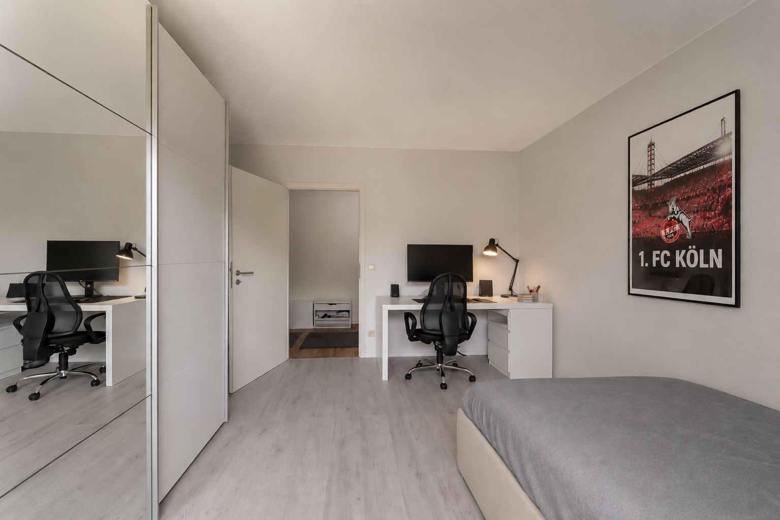Modernes Schlafzimmer mit Schreibtisch, Bürostuhl, Bett, großem Spiegel und Poster an der Wand.