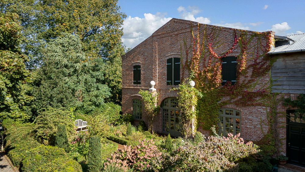 Backsteinwohnhaus mit Kletterpflanzen und Garten, umgeben von Bäumen und Sträuchern.