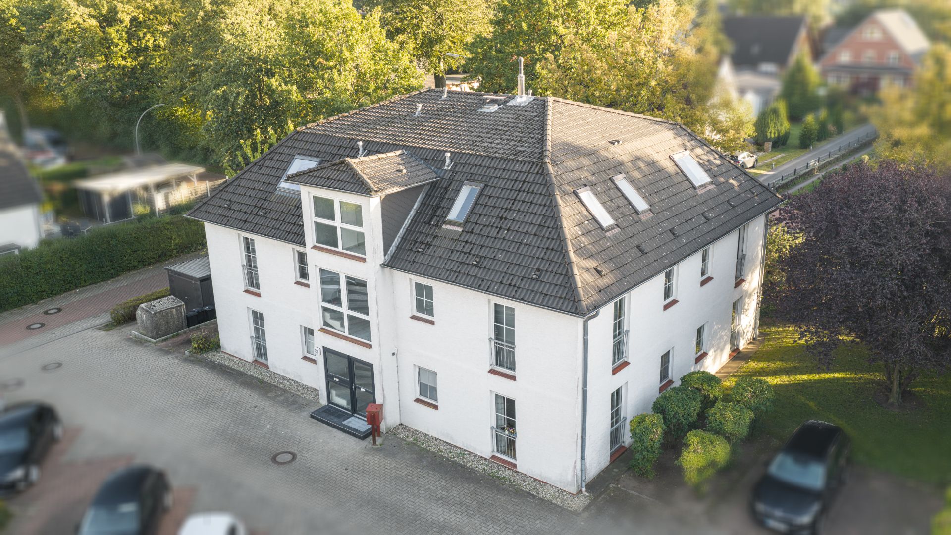 Zweistöckiges Wohnhaus mit Satteldach, mehreren Fenstern und geparkten Autos vor dem Gebäude.