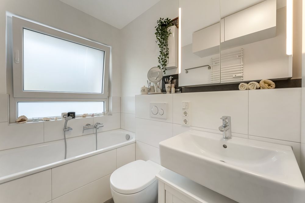 Modernes, weißes Badezimmer mit Badewanne, Waschbecken, Spiegel und Fenster.