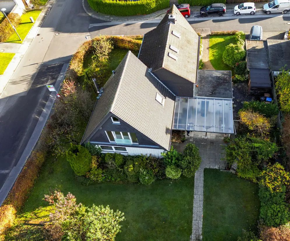 Luftaufnahme eines Einfamilienhauses mit Garten, Terrasse und angrenzender Straße.