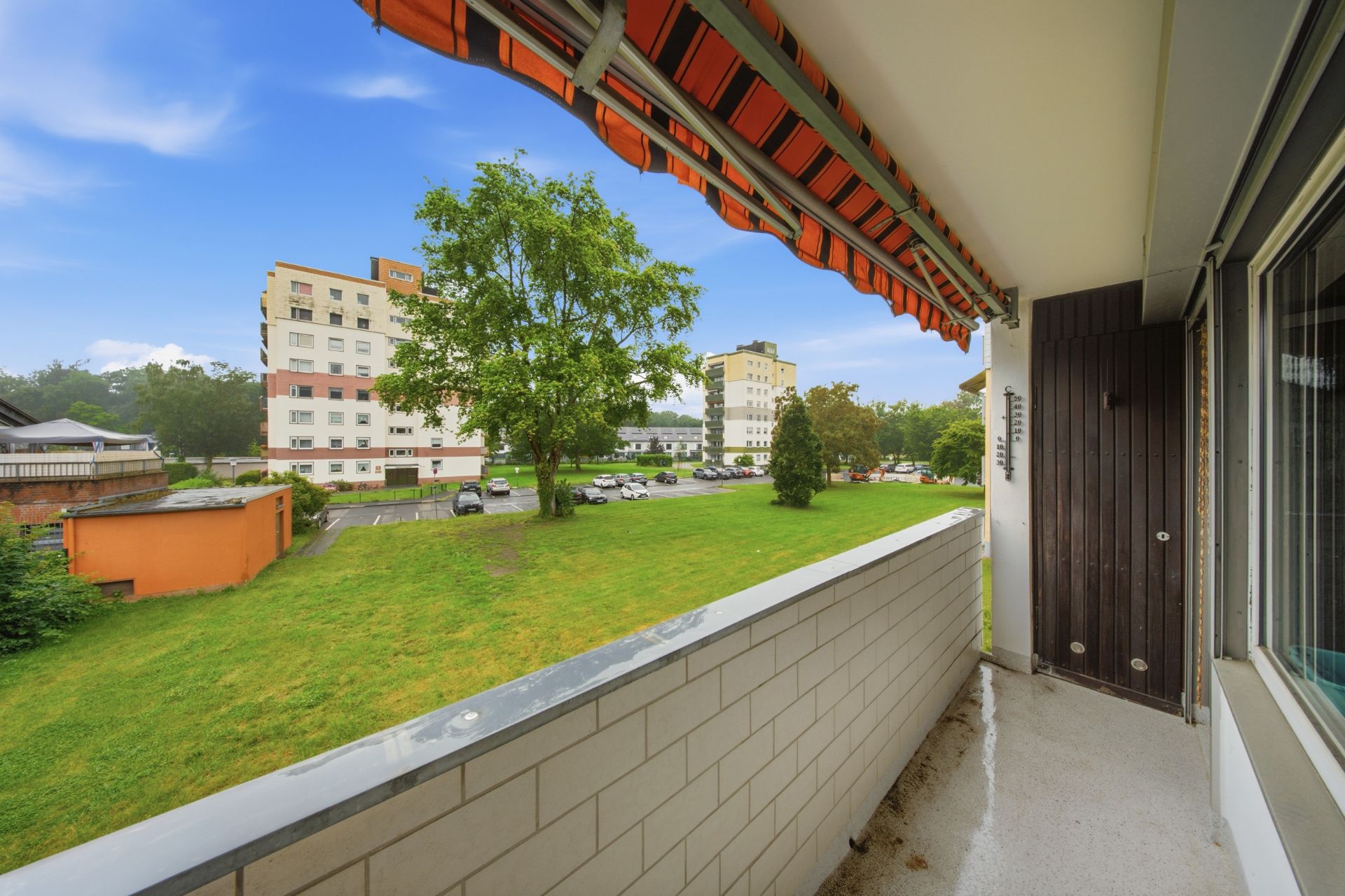 Balkon mit Markise, Blick auf Rasenfläche, Bäume und Wohnhäuser im Hintergrund.