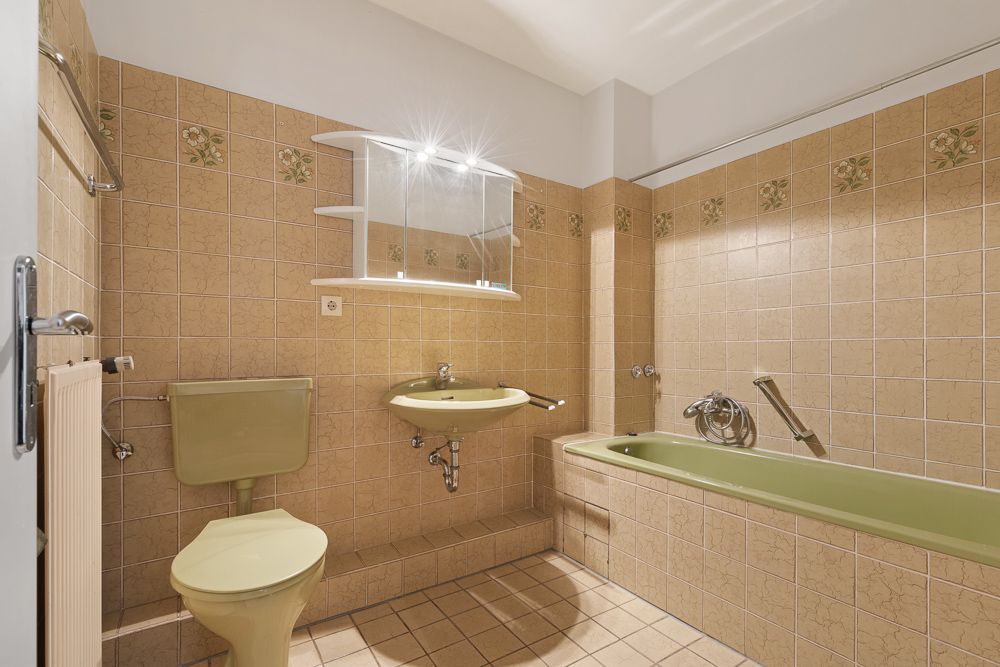 Badezimmer mit beigefarbenen Fliesen, grüner Toilette, Waschbecken und Badewanne.