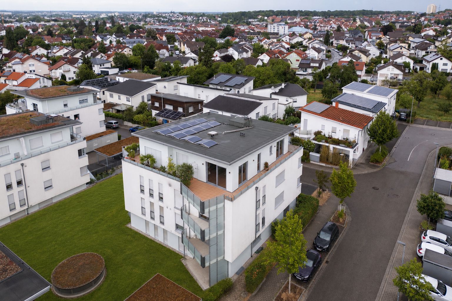 Mehrfamilienhaus mit Solarpanels auf dem Dach und umliegenden Wohnungen in einem Wohngebiet.