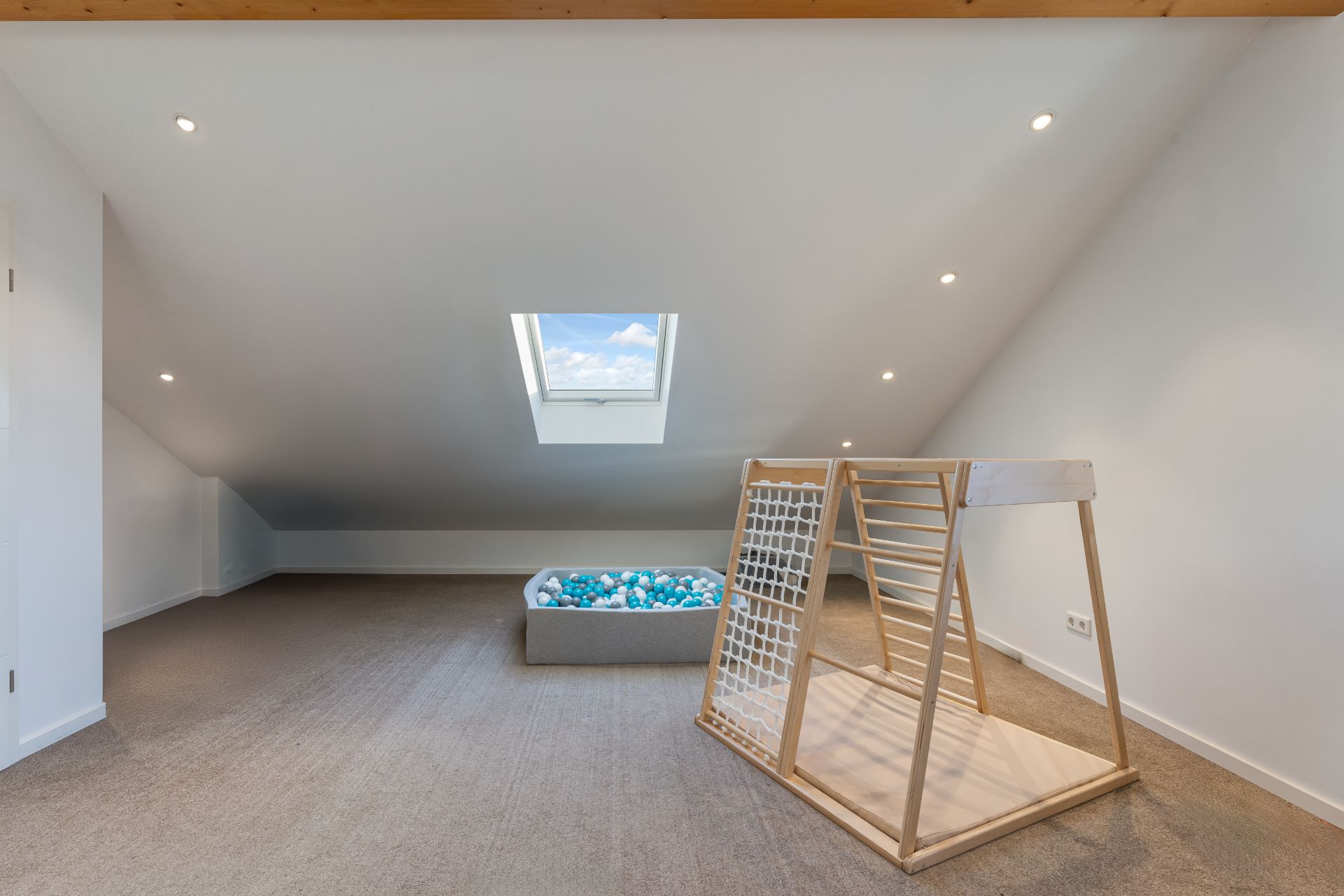 Dachgeschossraum mit Dachfenster, Holzklettergerüst und Bällebad auf Teppichboden.