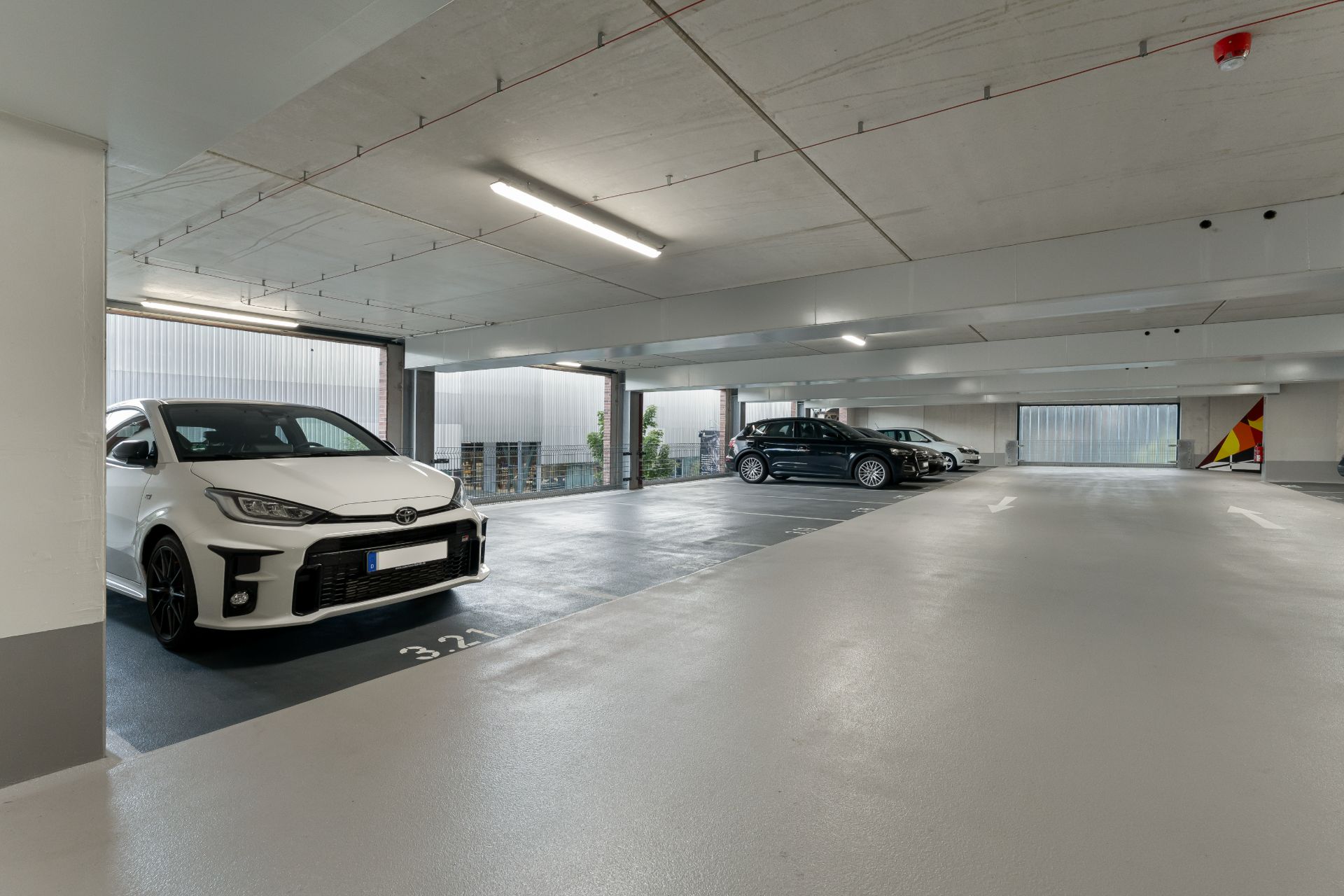 Helle Tiefgarage mit mehreren geparkten Autos, unter anderem einem weißen Auto im Vordergrund.