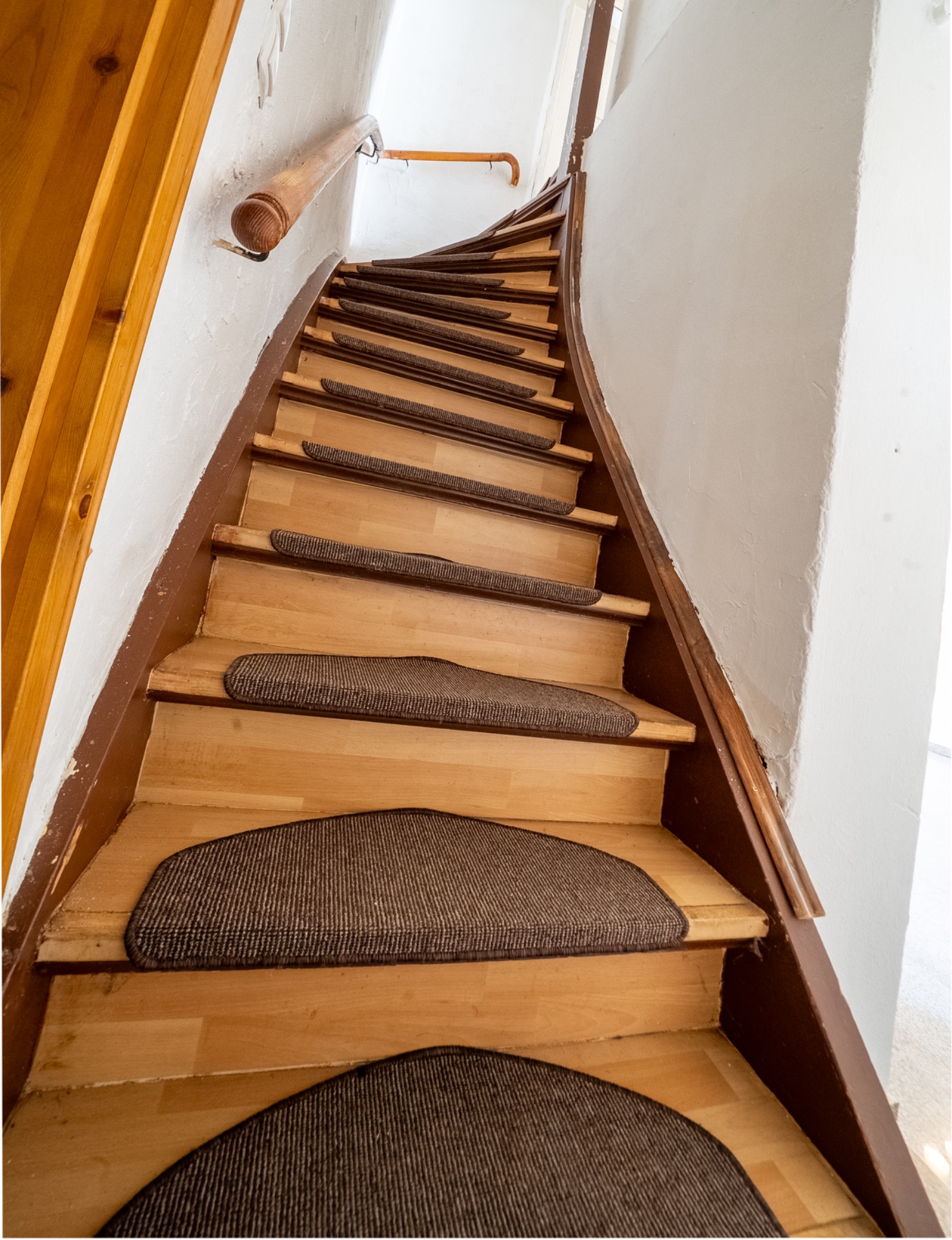 Holztreppe mit Teppichstufen und Geländer an einer weißen Wand.