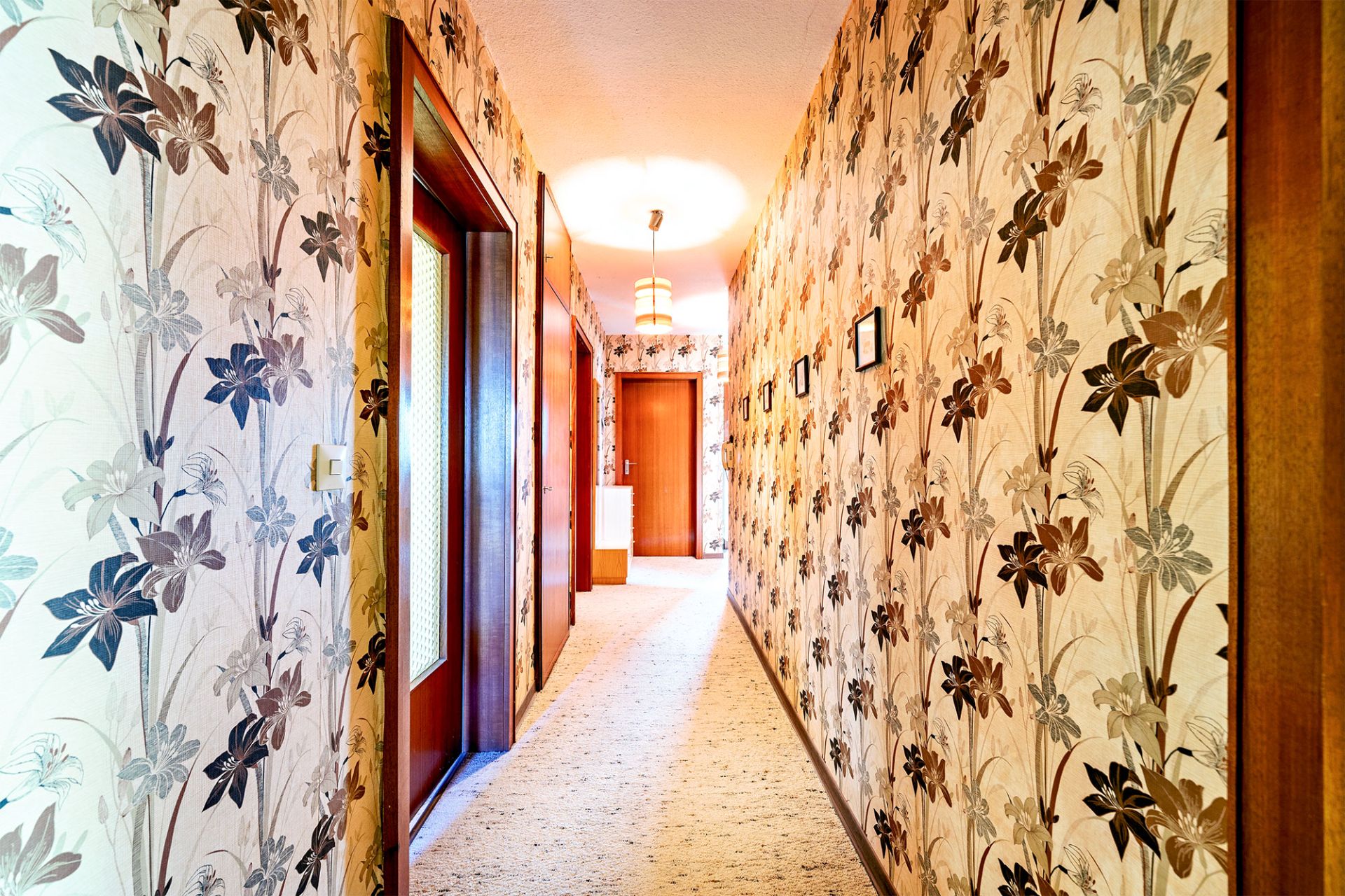 Langer Flur mit bunter Blumenmuster-Tapete und mehreren Holztüren.