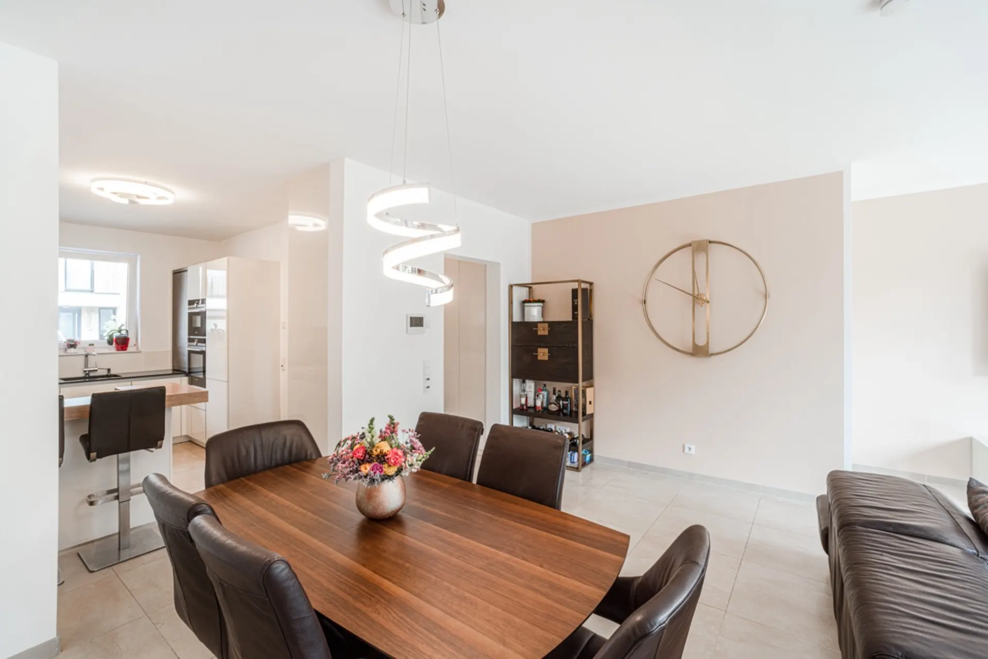 Essbereich mit Holztisch, braunen Stühlen, moderner Lampe und Blick in die offene Küche.