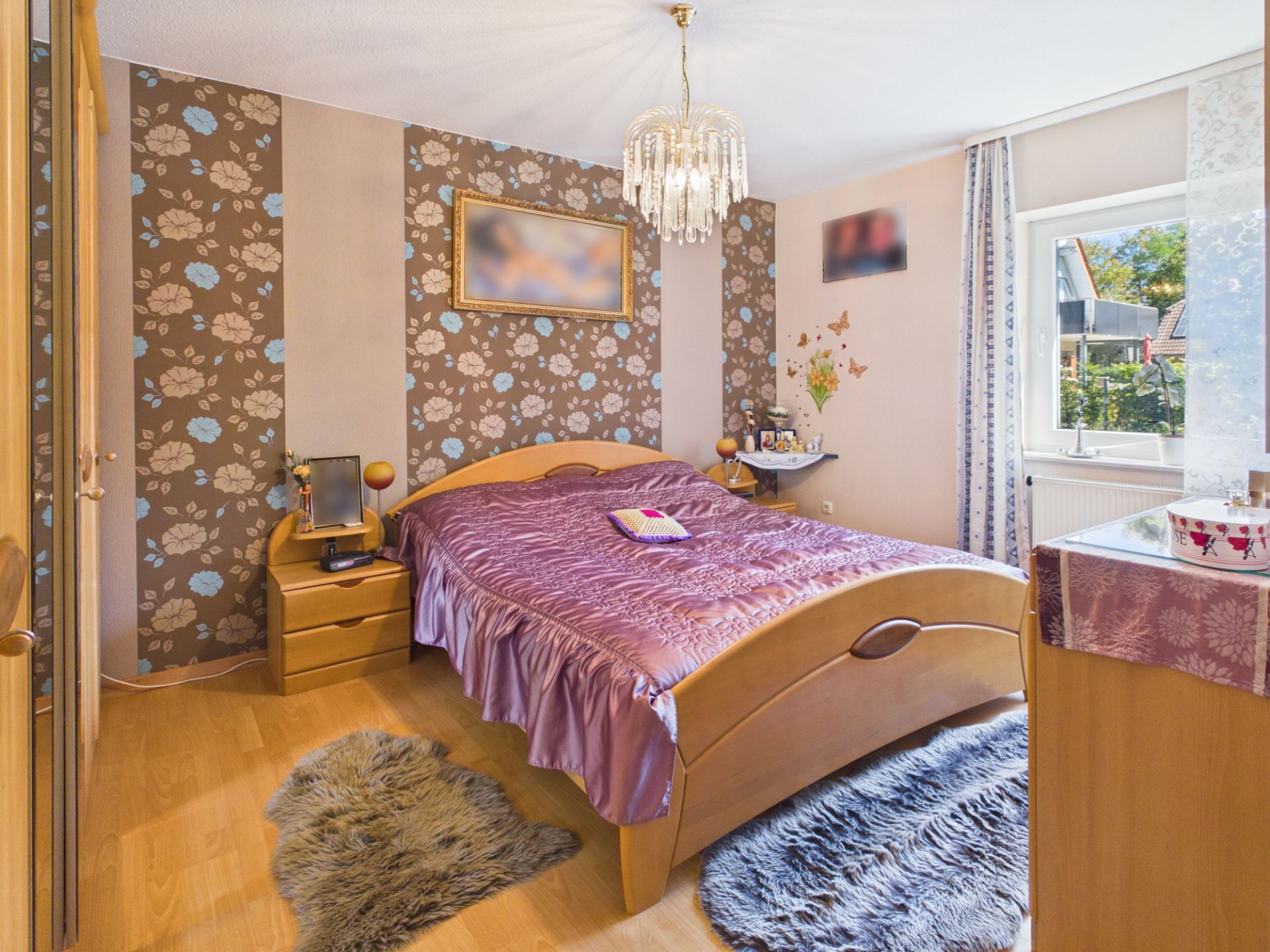 Schlafzimmer mit Doppelbett, Nachttischen, Teppich, Kronleuchter und Fenster mit Blick nach draußen.