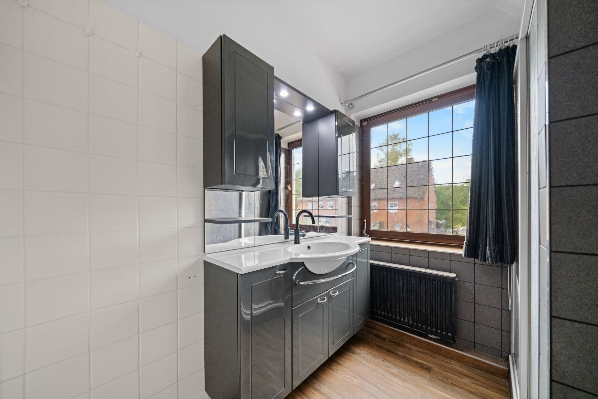 Modernes Badezimmer mit grauen Schränken, Waschbecken, großem Fenster und Holzboden.