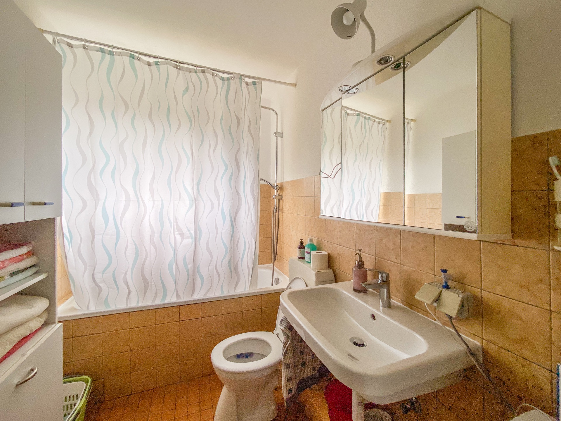 Helles Badezimmer mit Badewanne, Duschvorhang, Waschbecken, Spiegel und Toilette.