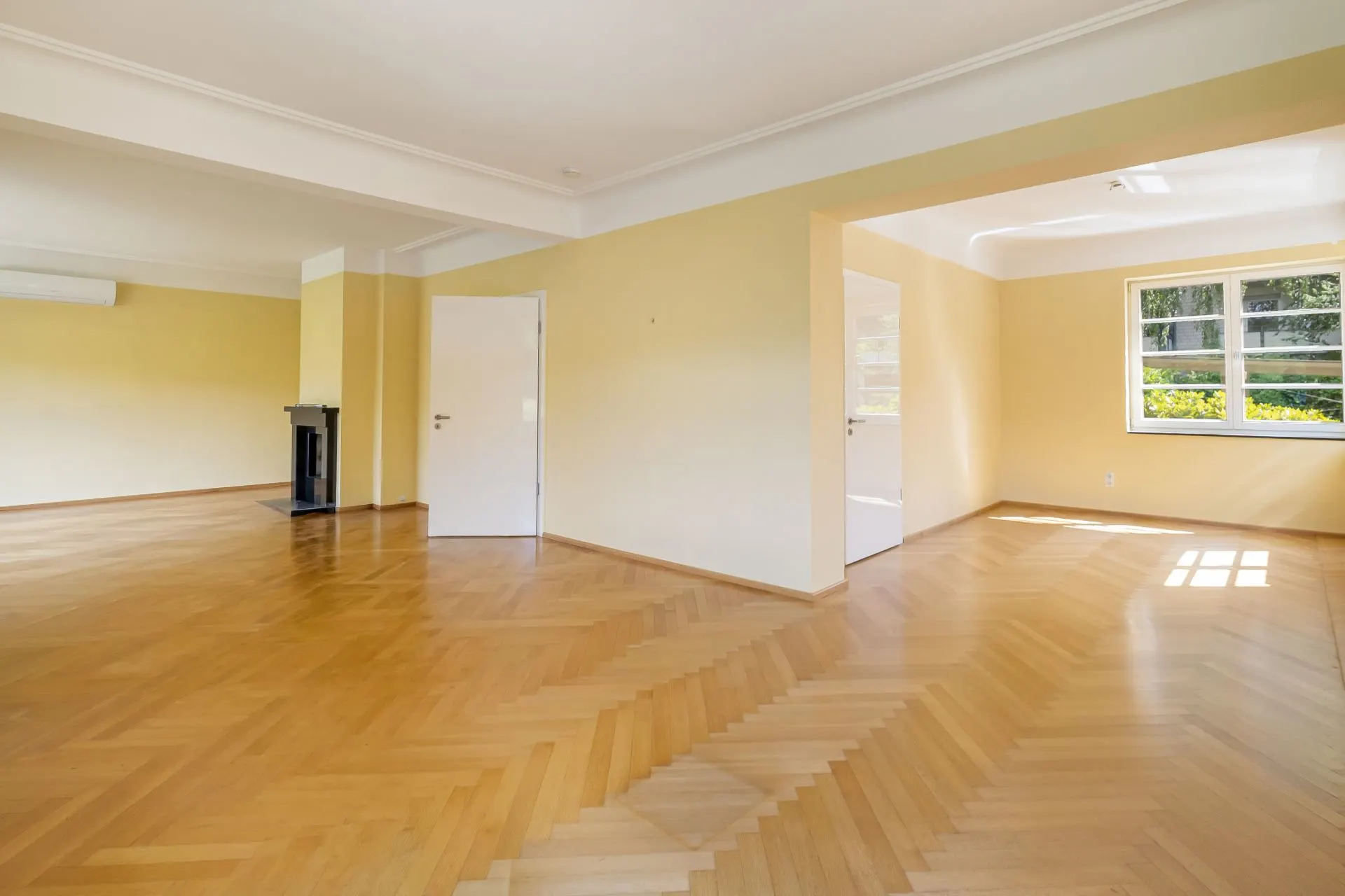 Heller Wohnraum mit Parkettboden, gelben Wänden und großen Fenstern.