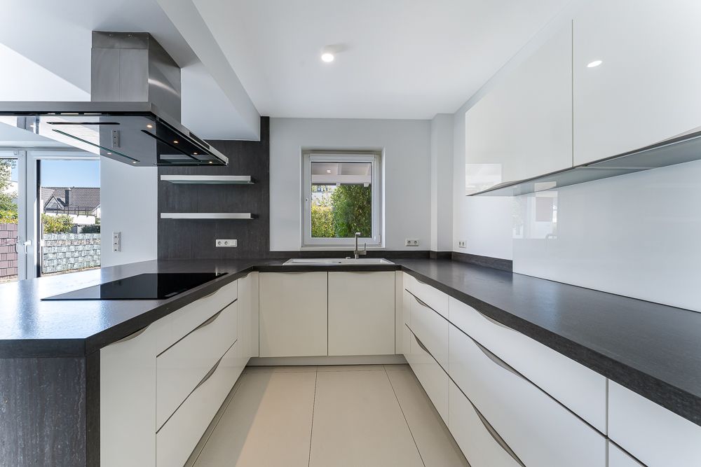 Moderne Küche mit weißen Schränken, dunkler Arbeitsplatte und Fenster über der Spüle.