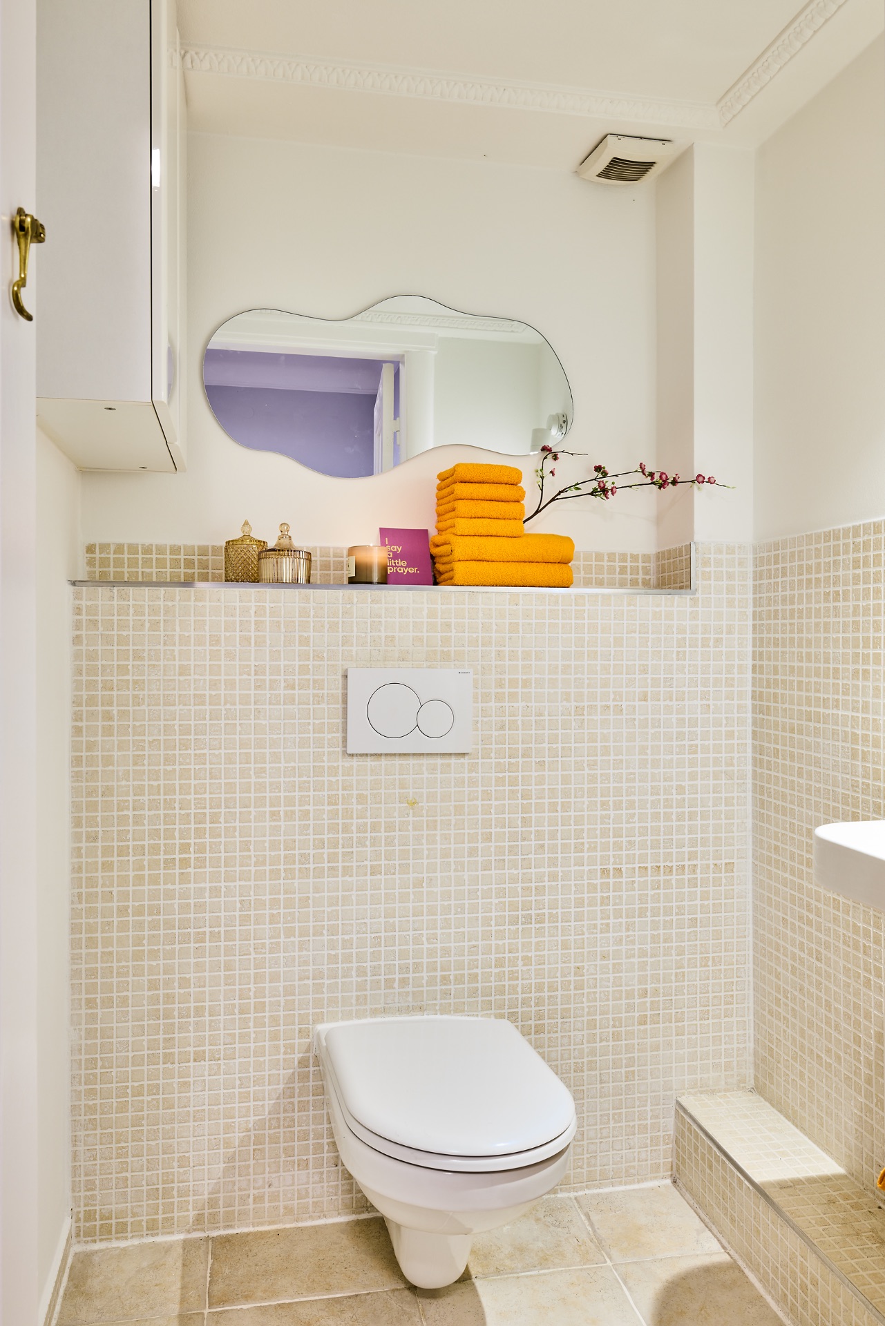 Modernes Badezimmer mit Wandtoilette, Spiegel und gelben Handtüchern auf Ablage.