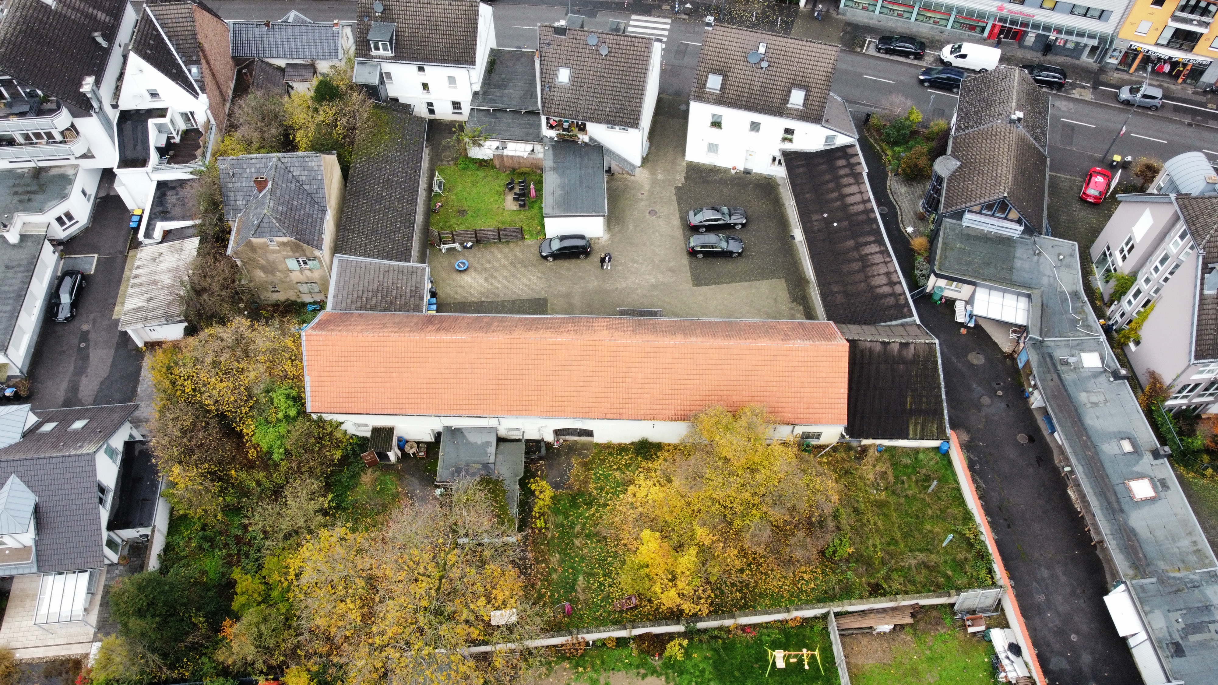 Luftaufnahme eines Wohngebäudes mit Innenhof, mehreren Autos und umgebendem Garten.