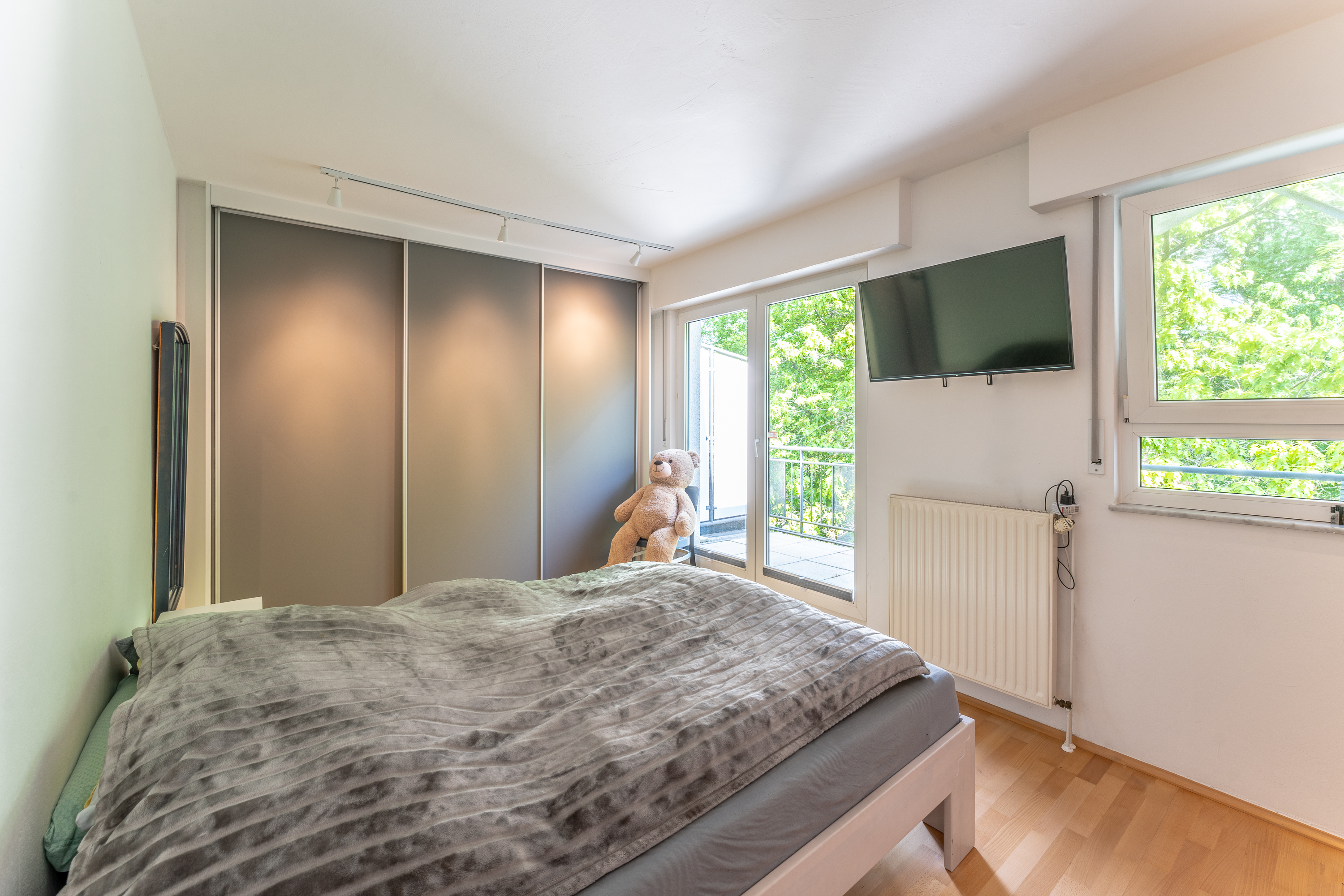 Schlafzimmer mit Doppelbett, grauem Schrank, Fernseher und großem Fenster mit Blick ins Grüne.