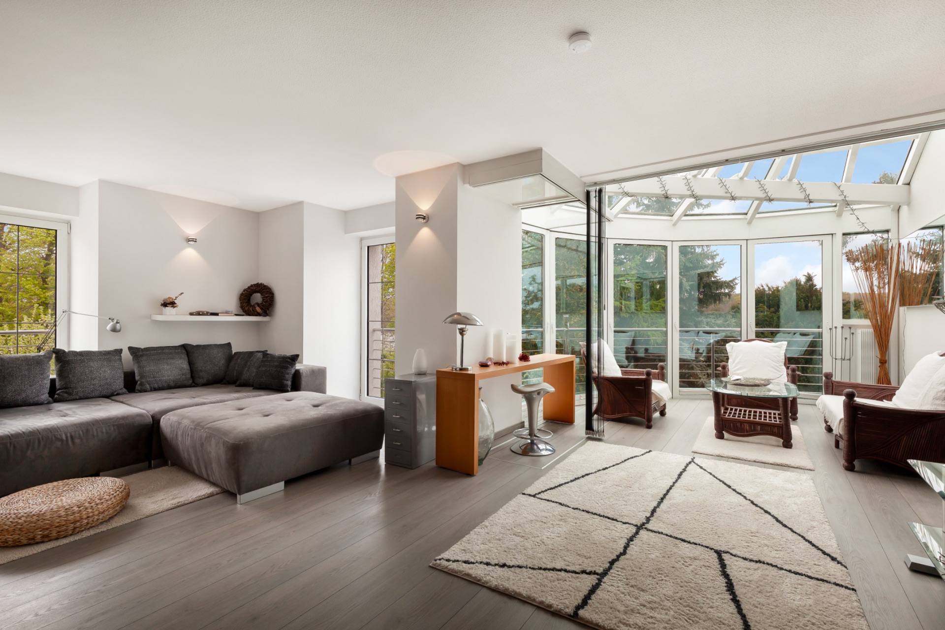 Helles Wohnzimmer mit großer Couch, Teppich und Wintergarten mit Glasfront.