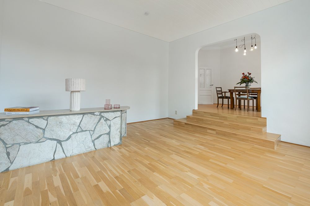 Helles Wohnzimmer mit Parkettboden, Steintisch und Stufen zum Essbereich.