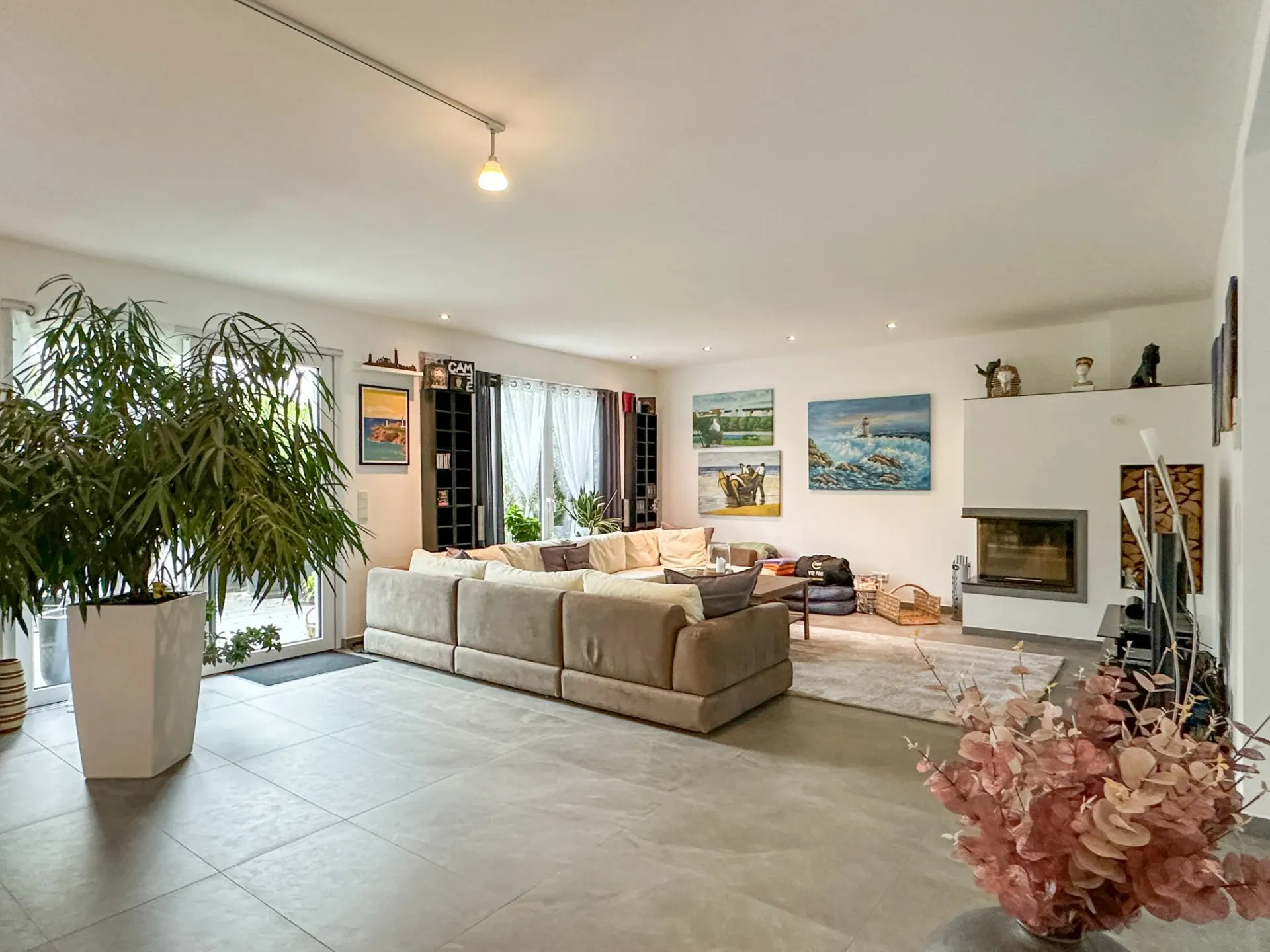 Helles Wohnzimmer mit großer Eckcouch, Pflanzen, Kamin und Bildern an der Wand.