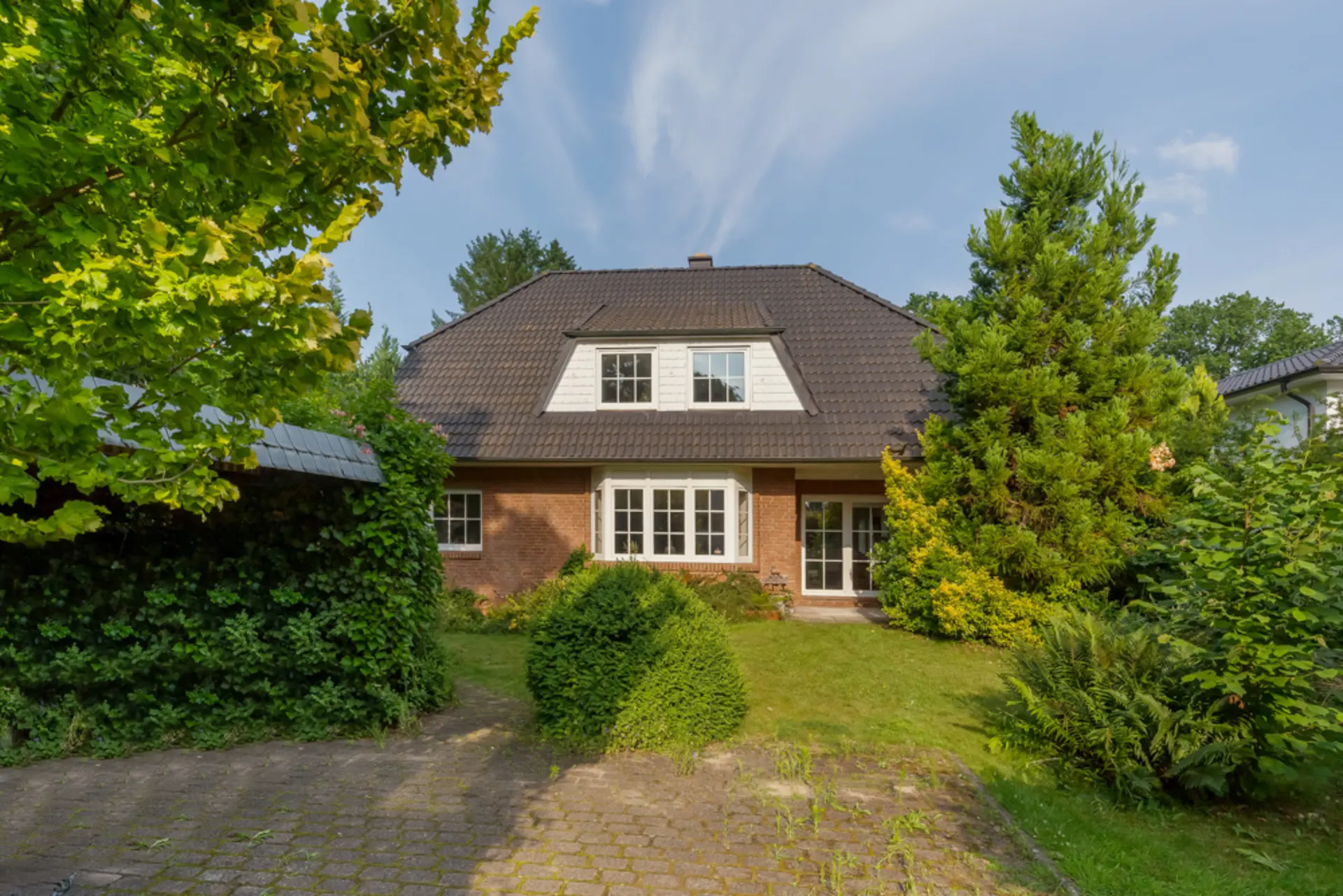Vorderansicht eines Einfamilienhauses mit Garten und gepflasterter Einfahrt.