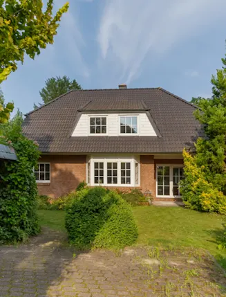 Vorderansicht eines Einfamilienhauses mit Garten und gepflasterter Einfahrt.