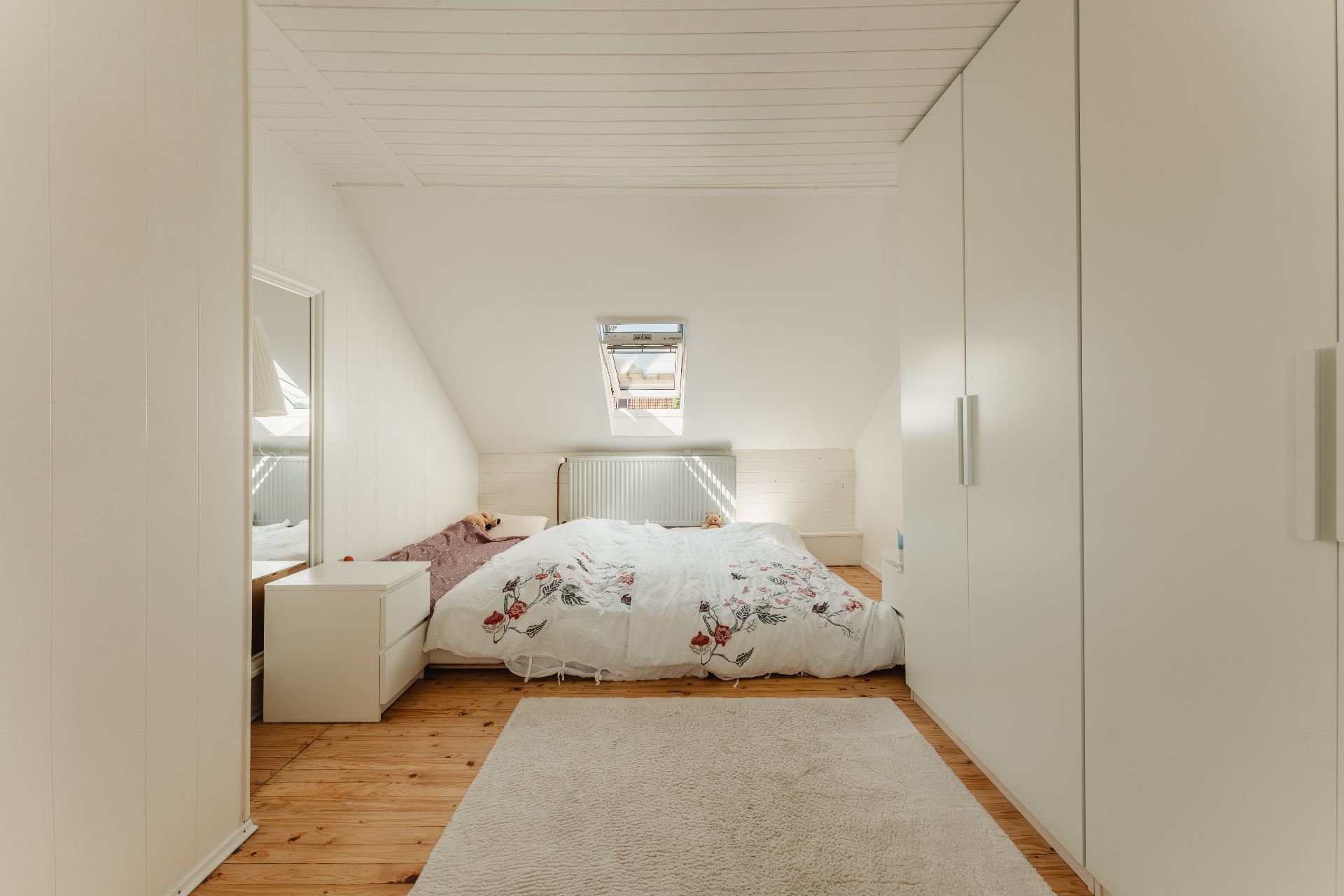 Helles Schlafzimmer im Dachgeschoss mit Doppelbett, Teppich und Einbauschränken.