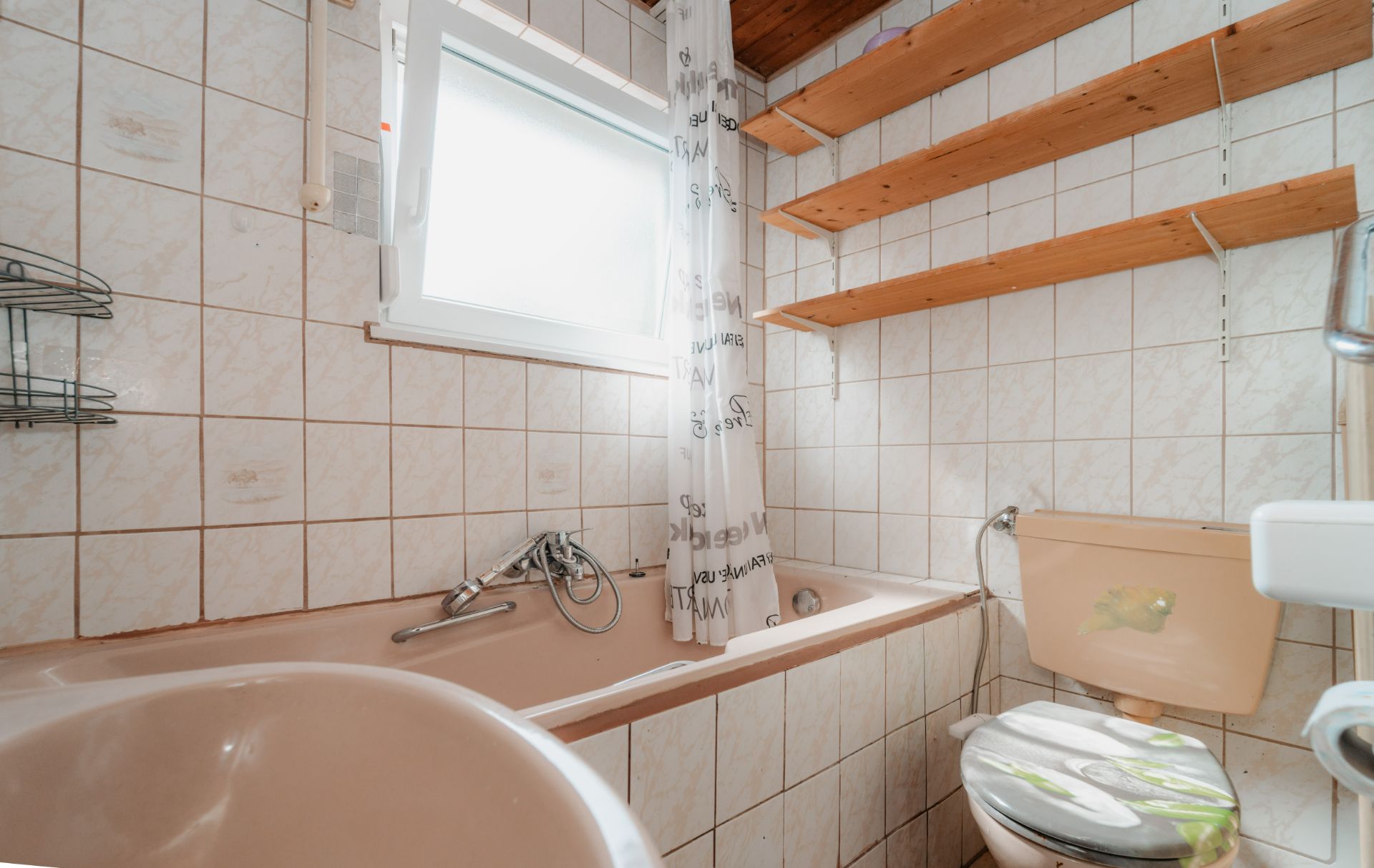 Kleines Badezimmer mit Badewanne, Toilette, Waschbecken und offenen Holzregalen an der Wand.