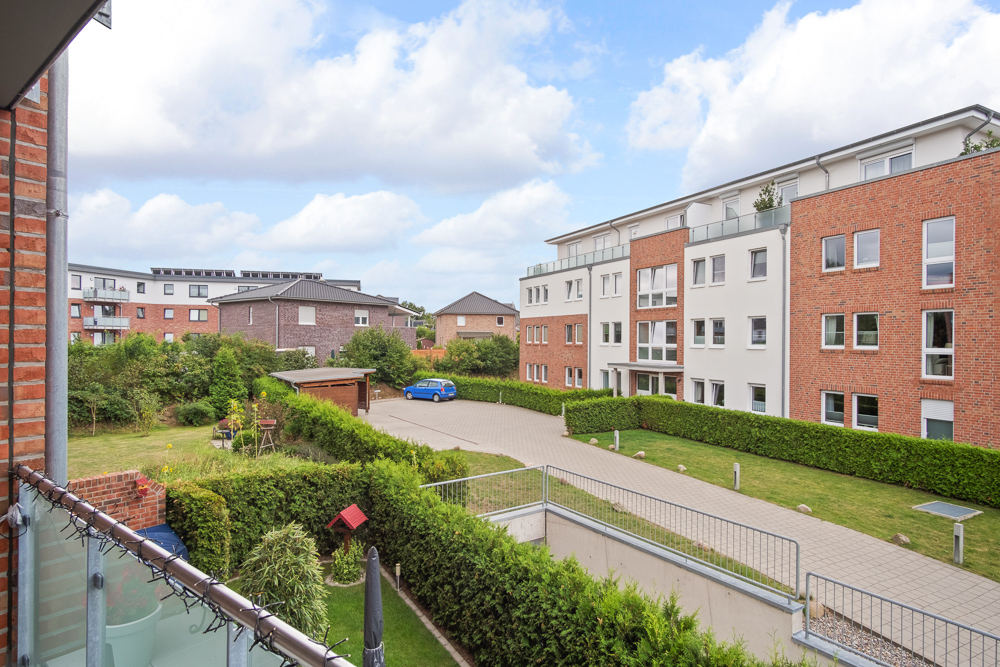 Blick vom Balkon auf einen Hof mit Wegen, Rasenflächen und Mehrfamilienhäusern.