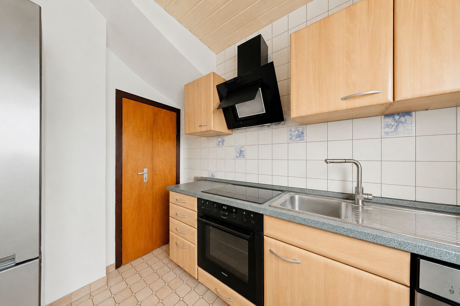 Helle Küche mit Holzfronten, Edelstahlspüle, Backofen und Dunstabzugshaube.