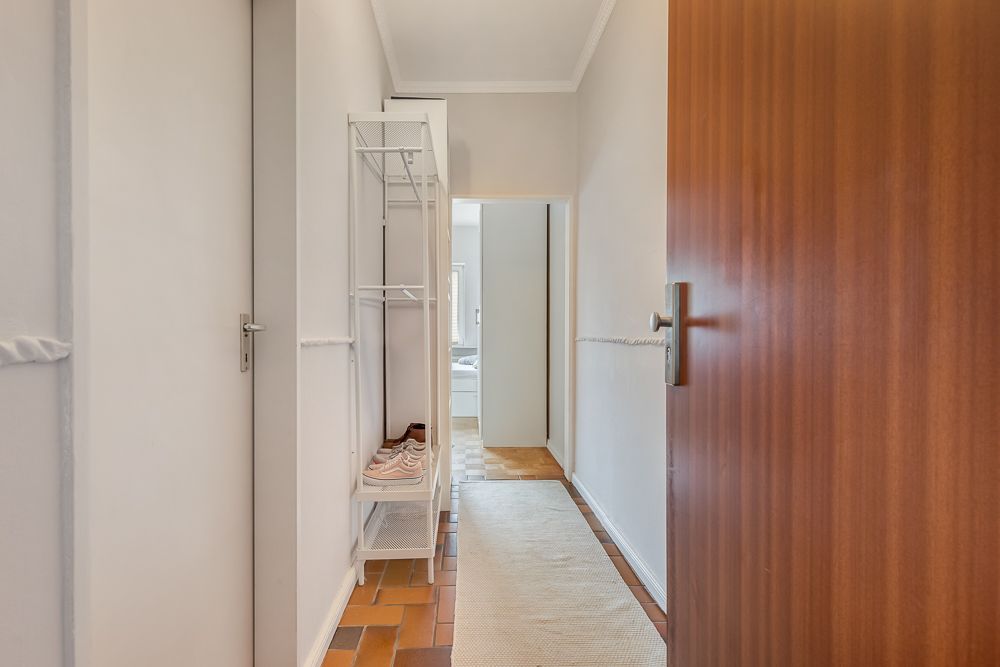 Heller Flur mit Holz- und Fliesenboden, Garderobe und geöffneter Tür.