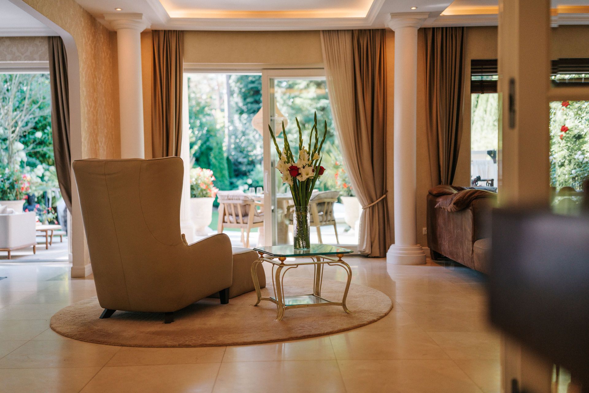 Helles Wohnzimmer mit Sessel, Glastisch und Blick auf Terrasse mit Garten.