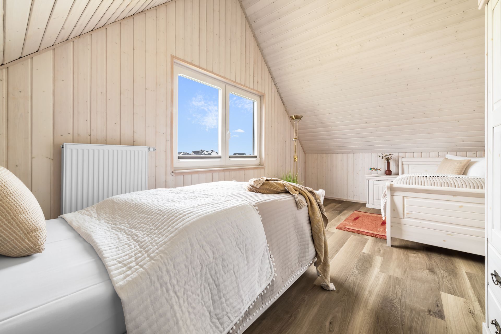 Helles Schlafzimmer mit zwei Einzelbetten, Holzdecke und großem Fenster.