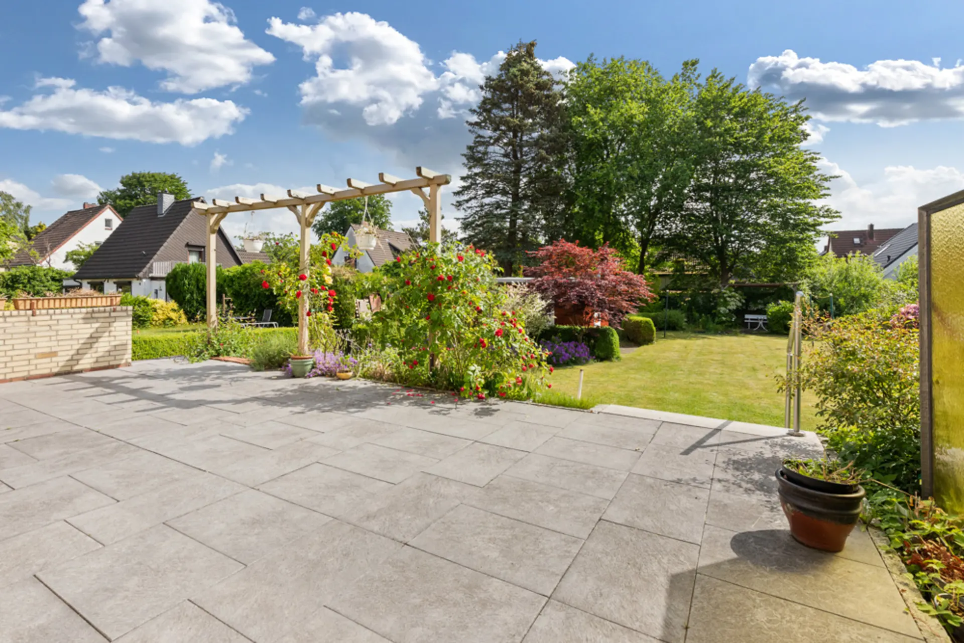 Große Terrasse mit Fliesen, Blumenbeeten und Rasenfläche in einem Wohnhausgarten.