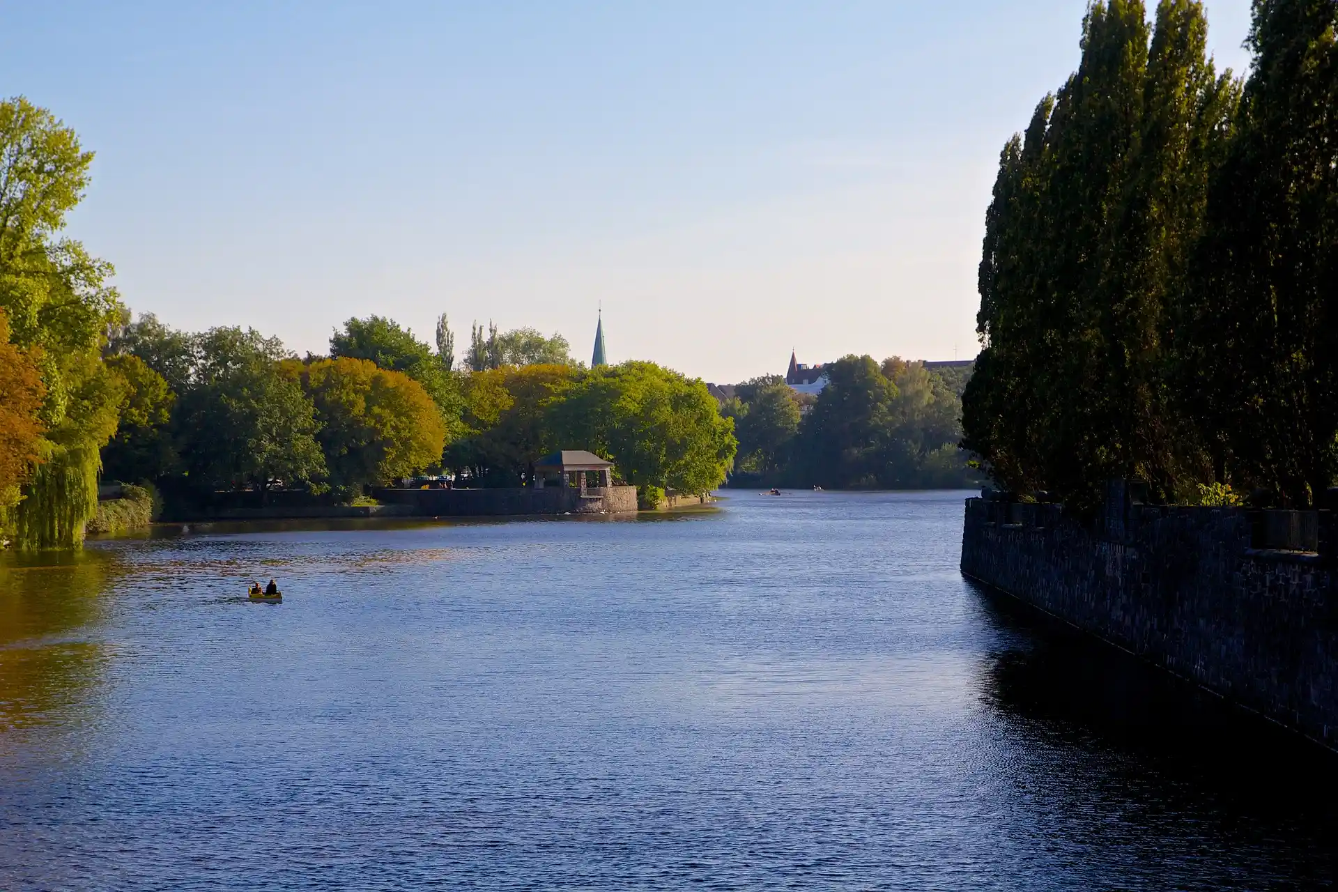 Fluss mit Bäumen am Ufer und einem kleinen Boot auf dem Wasser bei Tageslicht.