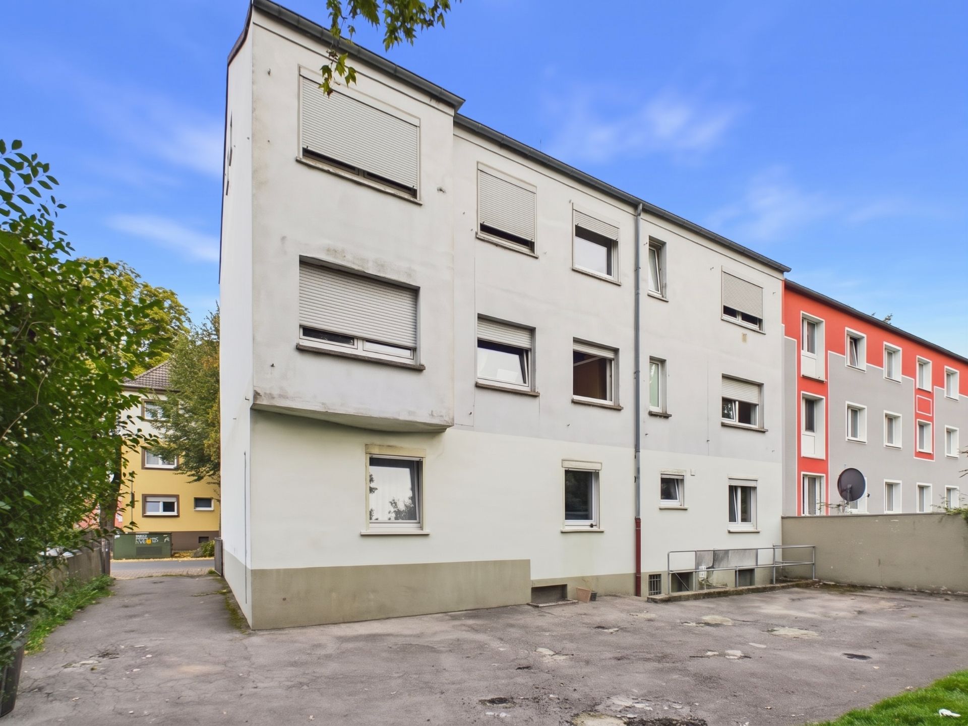 Dreistöckiges Wohnhaus mit mehreren Fenstern und einem Hof, teilweise mit Rollläden.