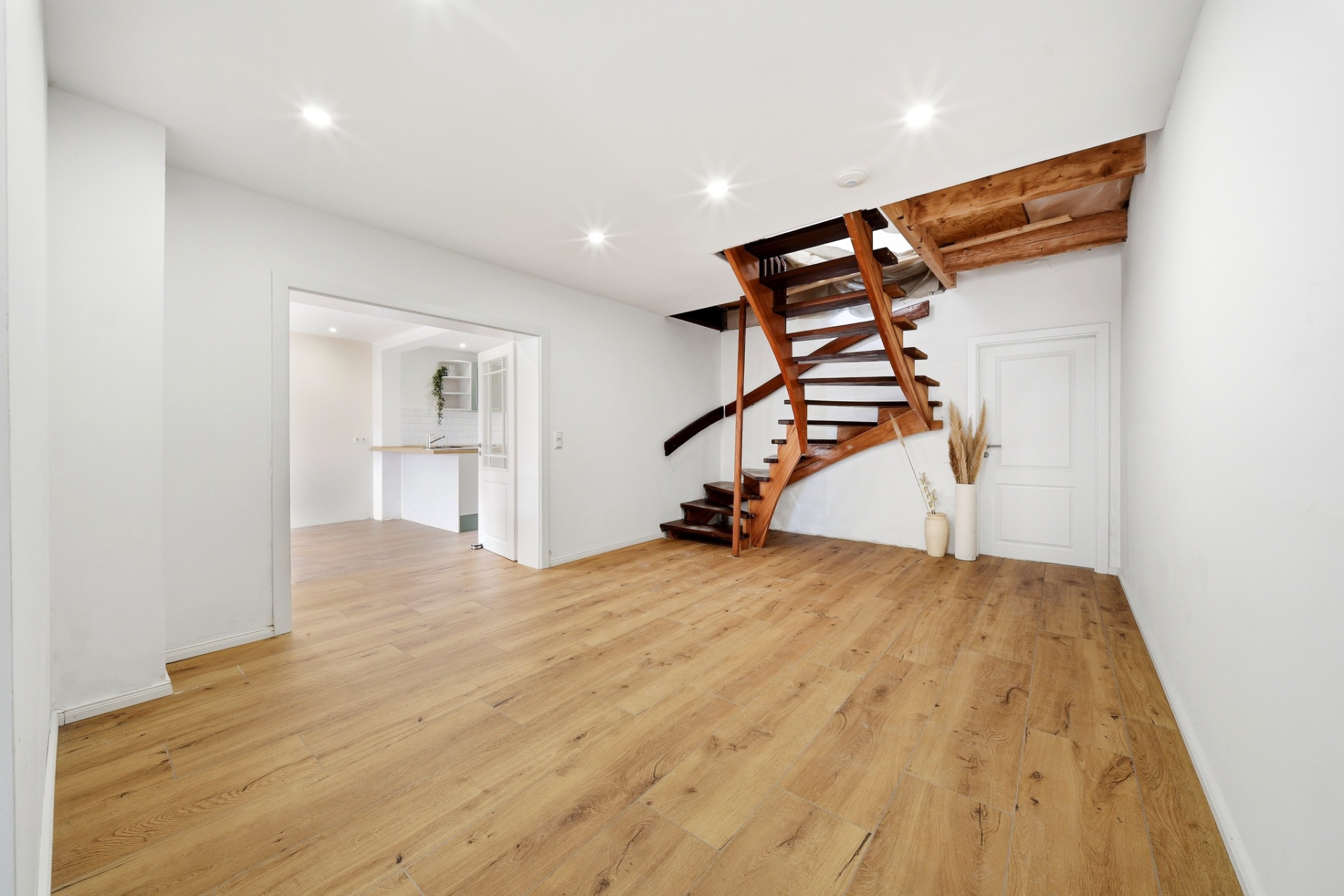 Heller Raum mit Holzfußboden, moderner Holzwendeltreppe und weißen Wänden.