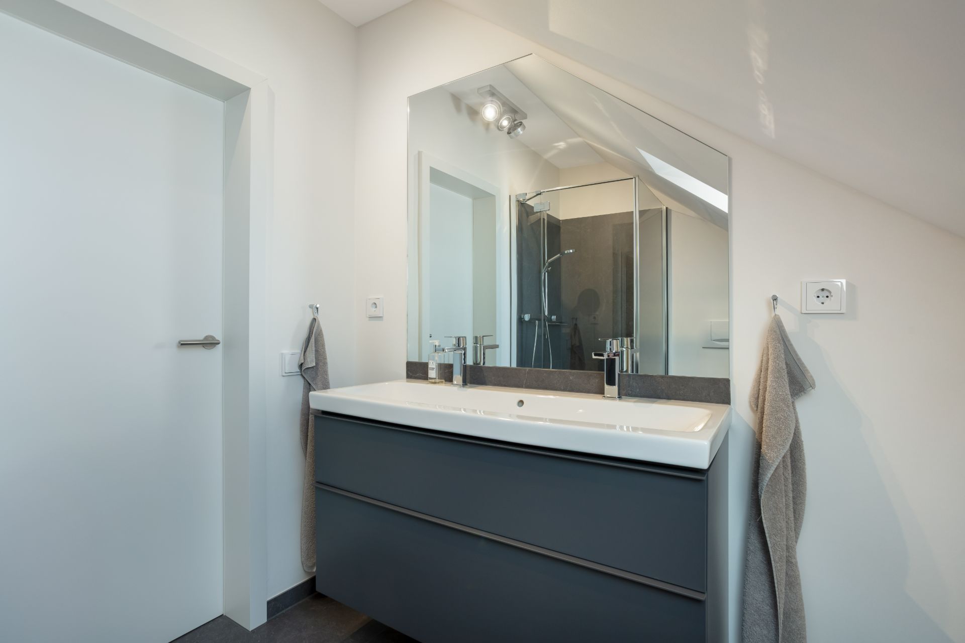 Modernes Badezimmer mit Doppelwaschbecken, großem Spiegel und zwei grauen Handtüchern an den Wänden.
