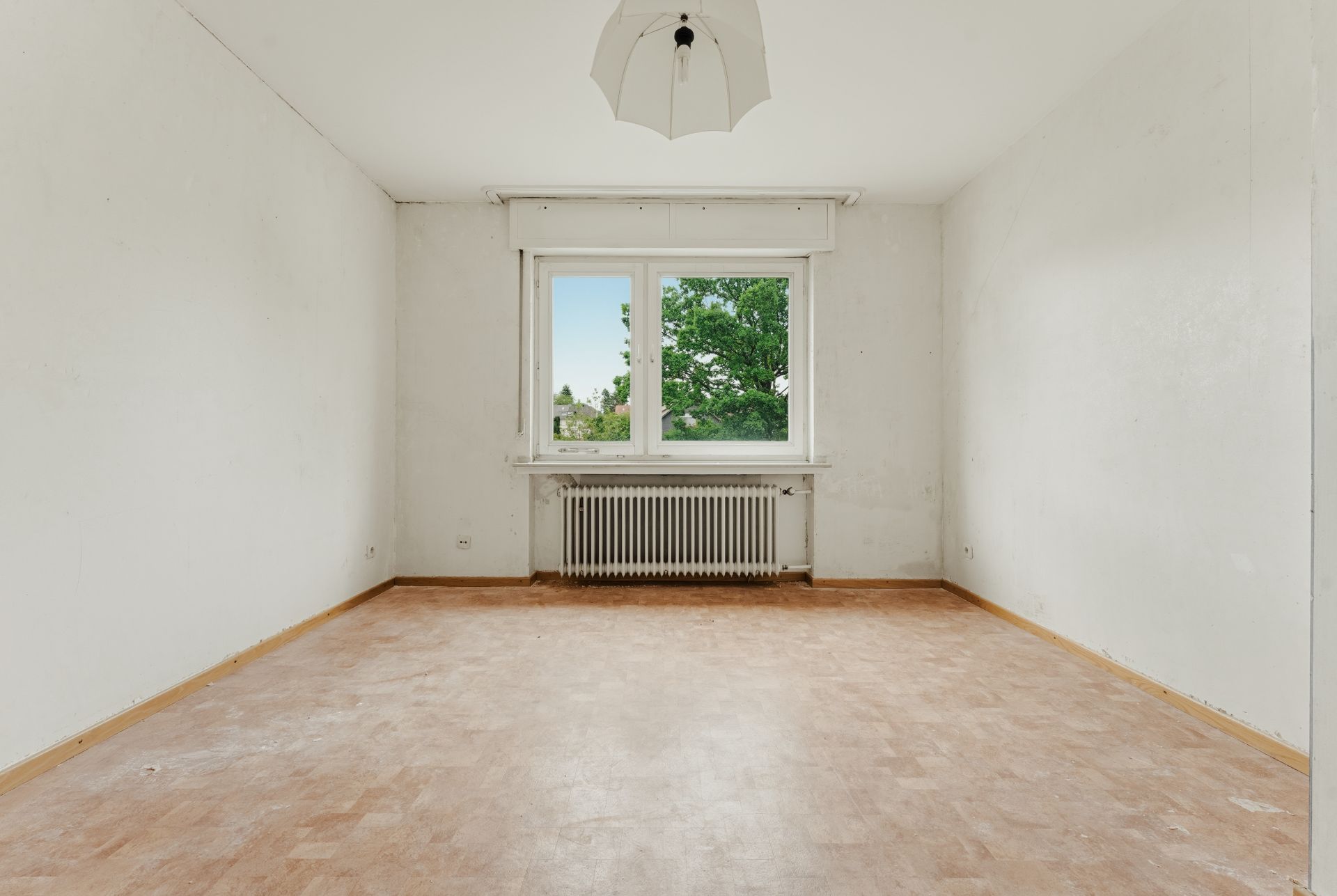Leerer Raum mit Fenster, Heizkörper und heller Deckenlampe, heller Boden.