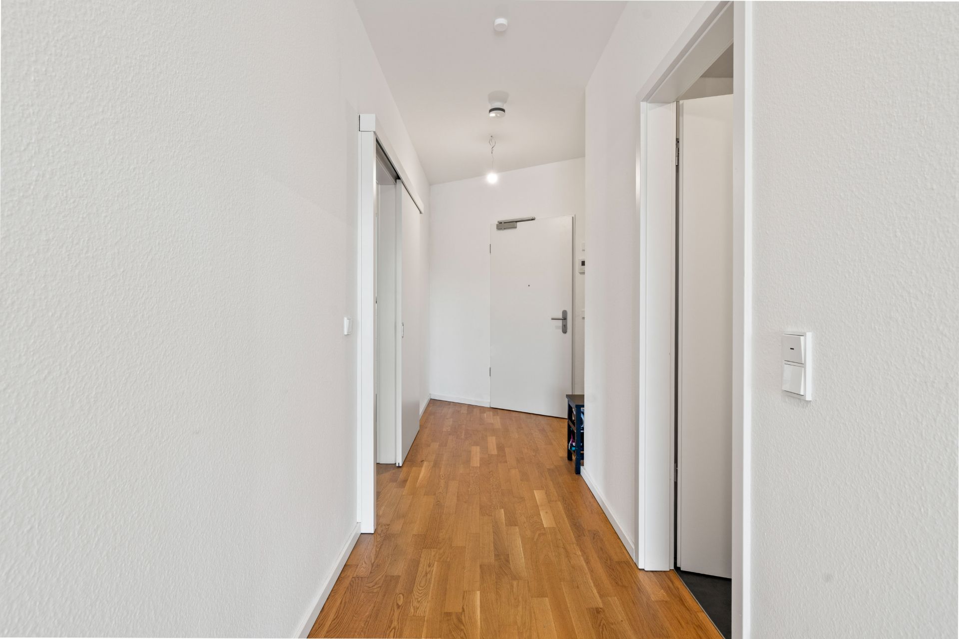 Heller Flur mit Holzboden, weißen Wänden und mehreren Türen in einer Wohnung.