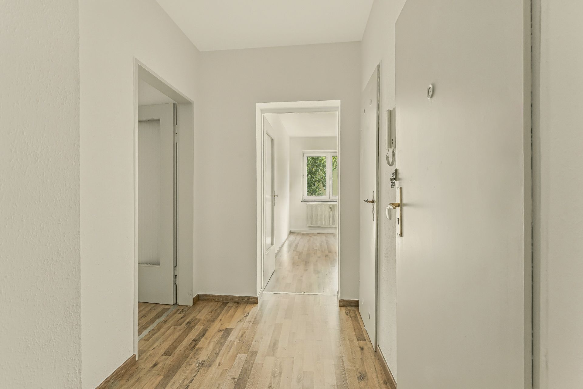 Heller Flur einer Wohnung mit Holzboden und mehreren offenstehenden Türen.