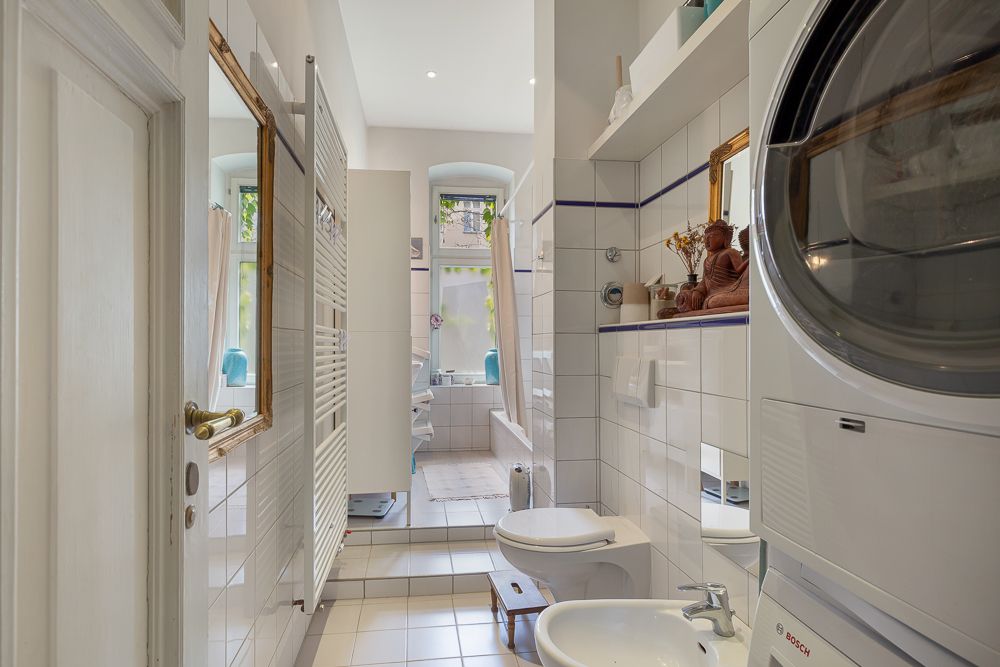 Helles Badezimmer mit Waschmaschine, Trockner, Badewanne, Bidet und Fenster.