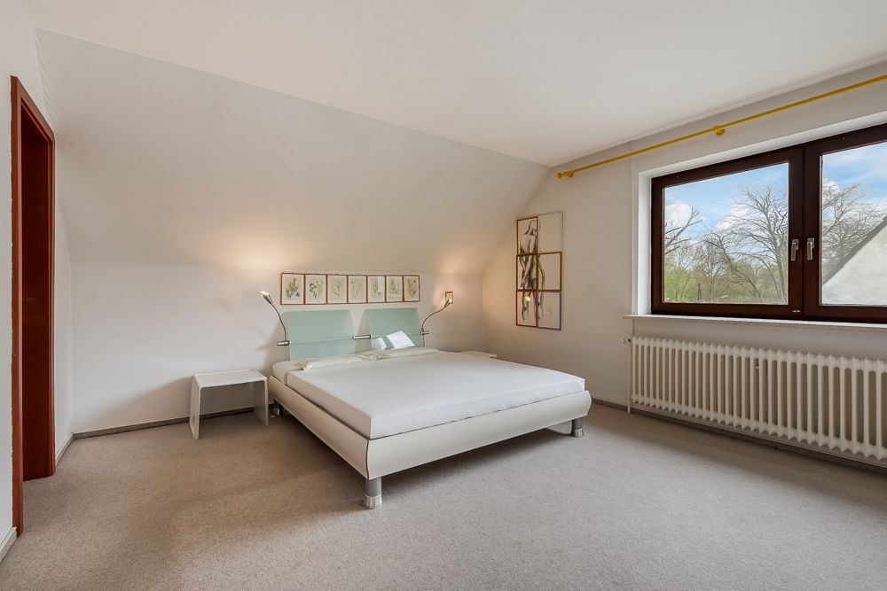 Helles Schlafzimmer mit Doppelbett, Nachttischen, Wandbildern und großem Fenster.