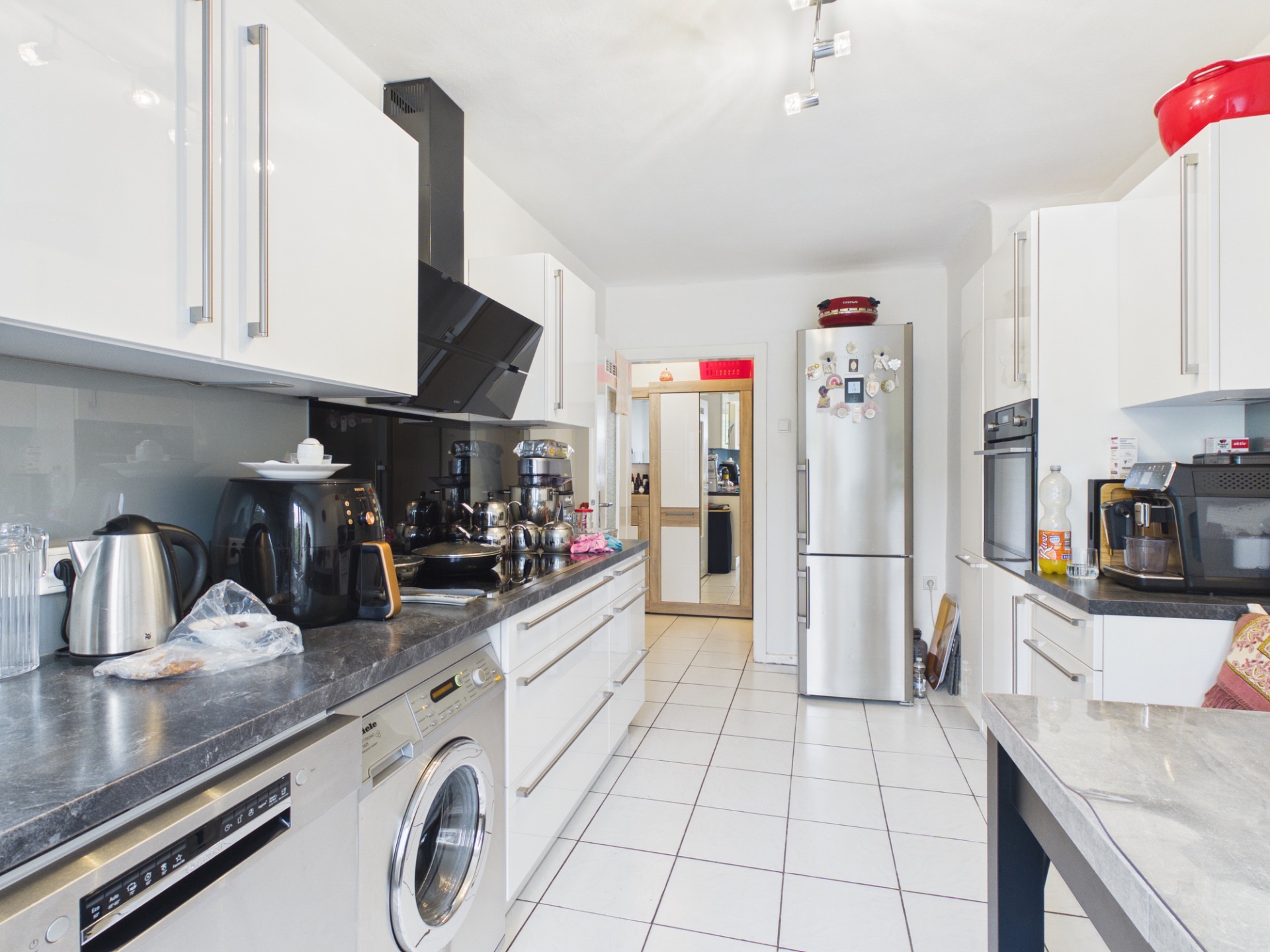 Moderne Küche mit weißen Schränken, Geräten, Waschmaschine und gefliestem Boden.