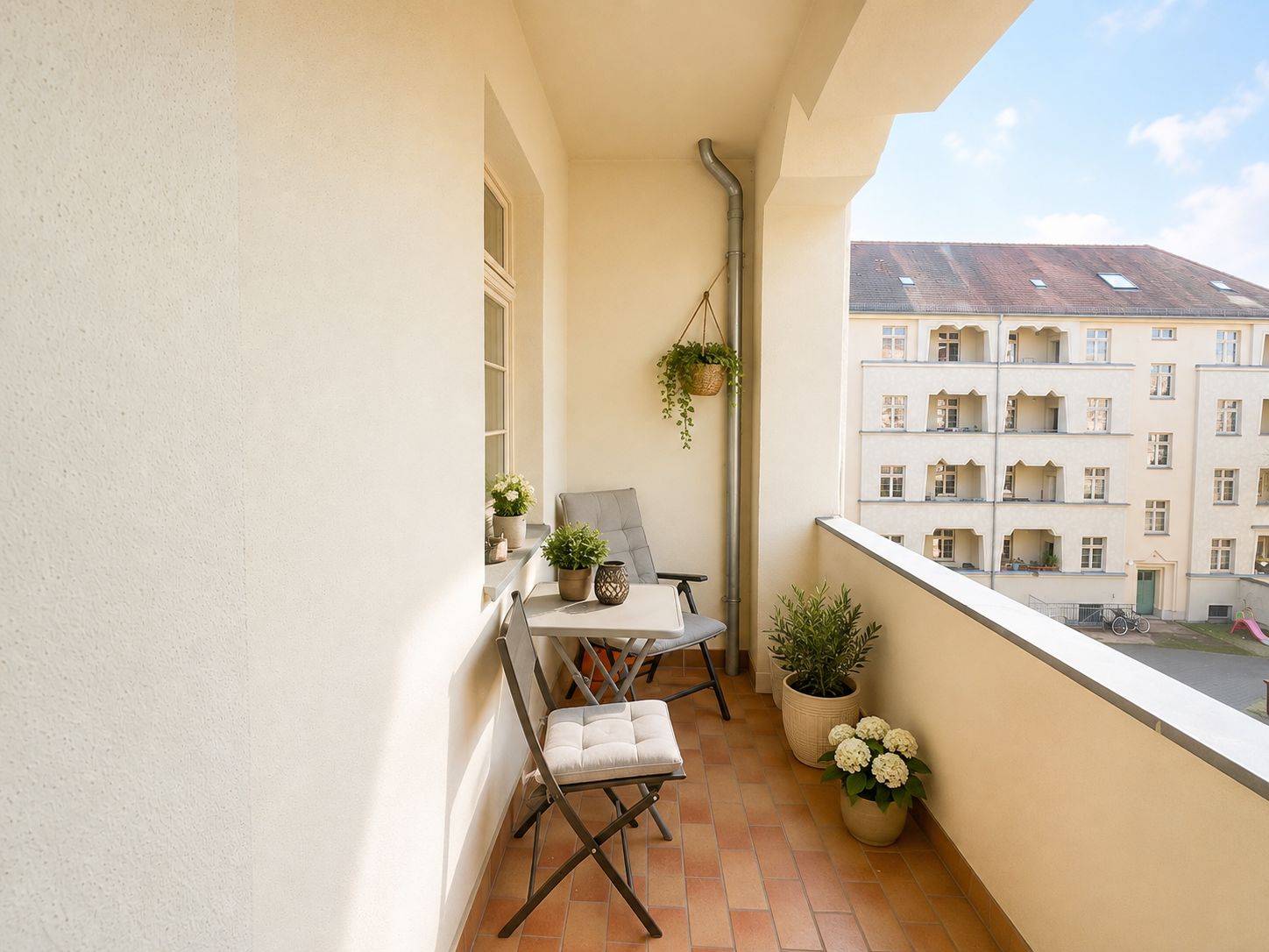 Heller Balkon mit zwei Stühlen, einem kleinen Tisch und mehreren Pflanzen in Töpfen.