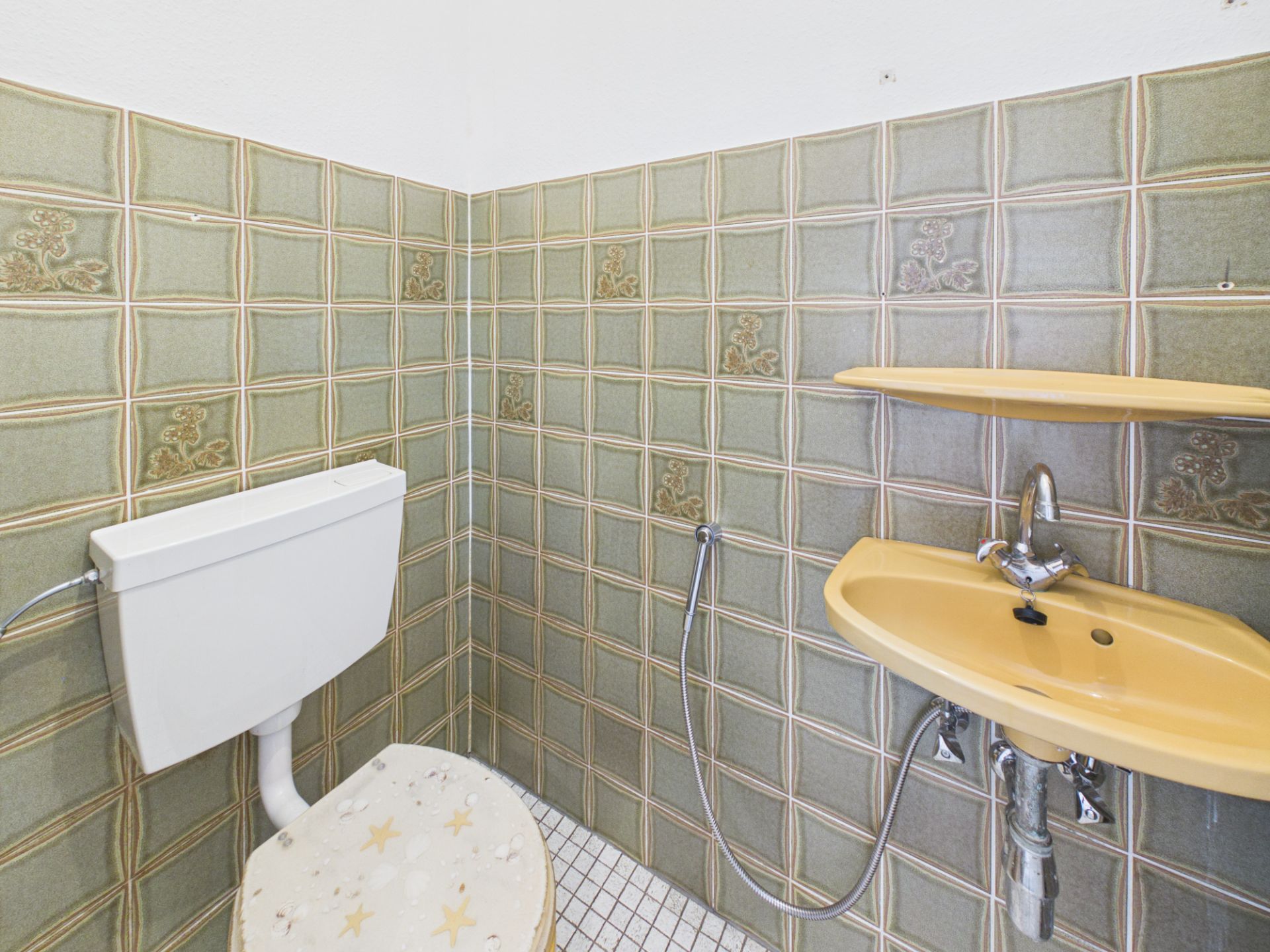 Kleines Bad mit grünen Fliesen, gelbem Waschbecken, WC und Regal.